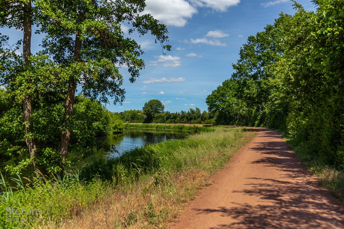 Ein Sandweg führt an einem See vorbei.