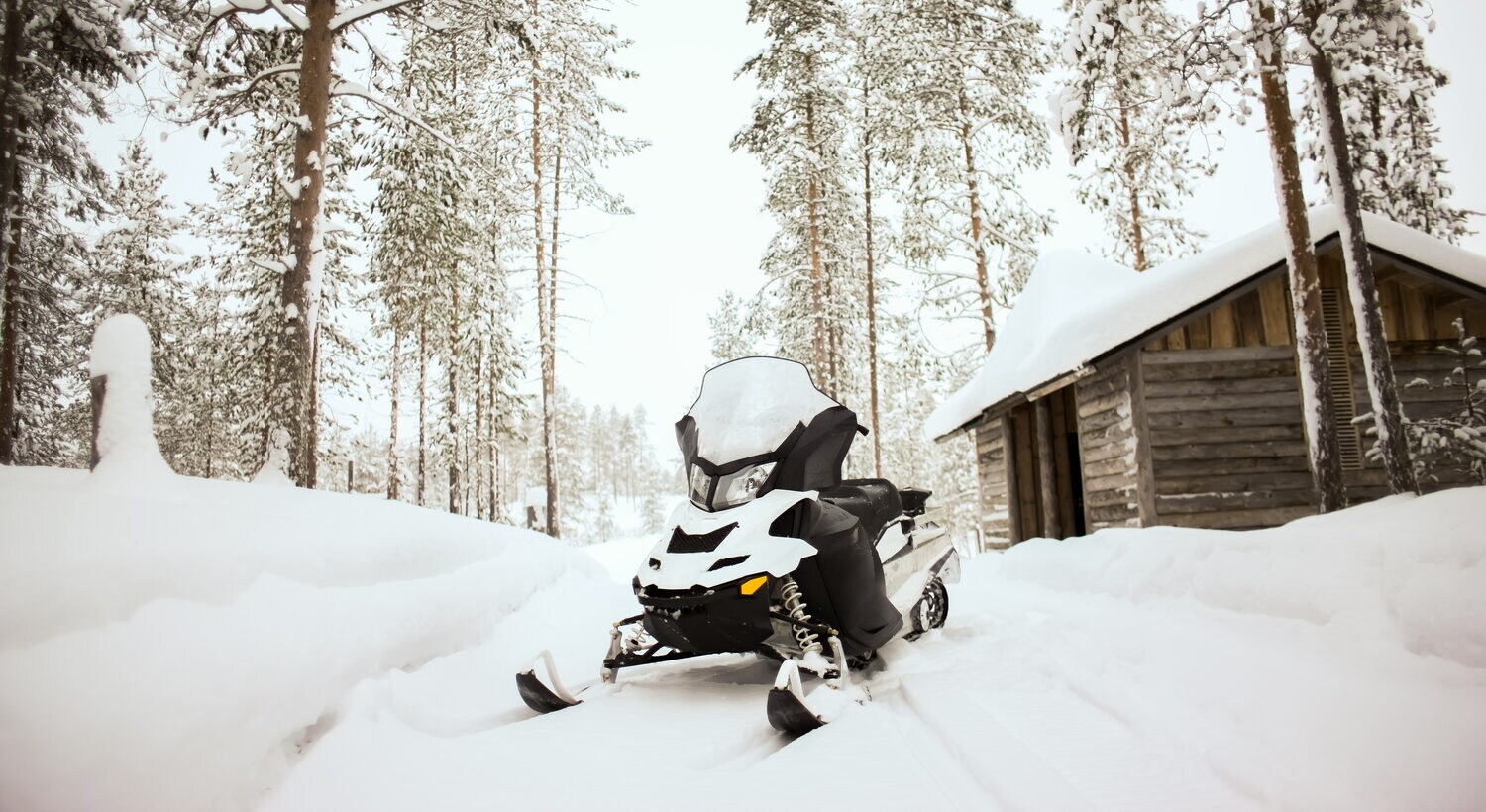 Ein Schneemobil steht auf einem schneebedeckten Weg vor einer kleinen Holzhütte Ein Schneemobil steht auf einem schneebedeckten Weg vor einer kleinen Holzhütte