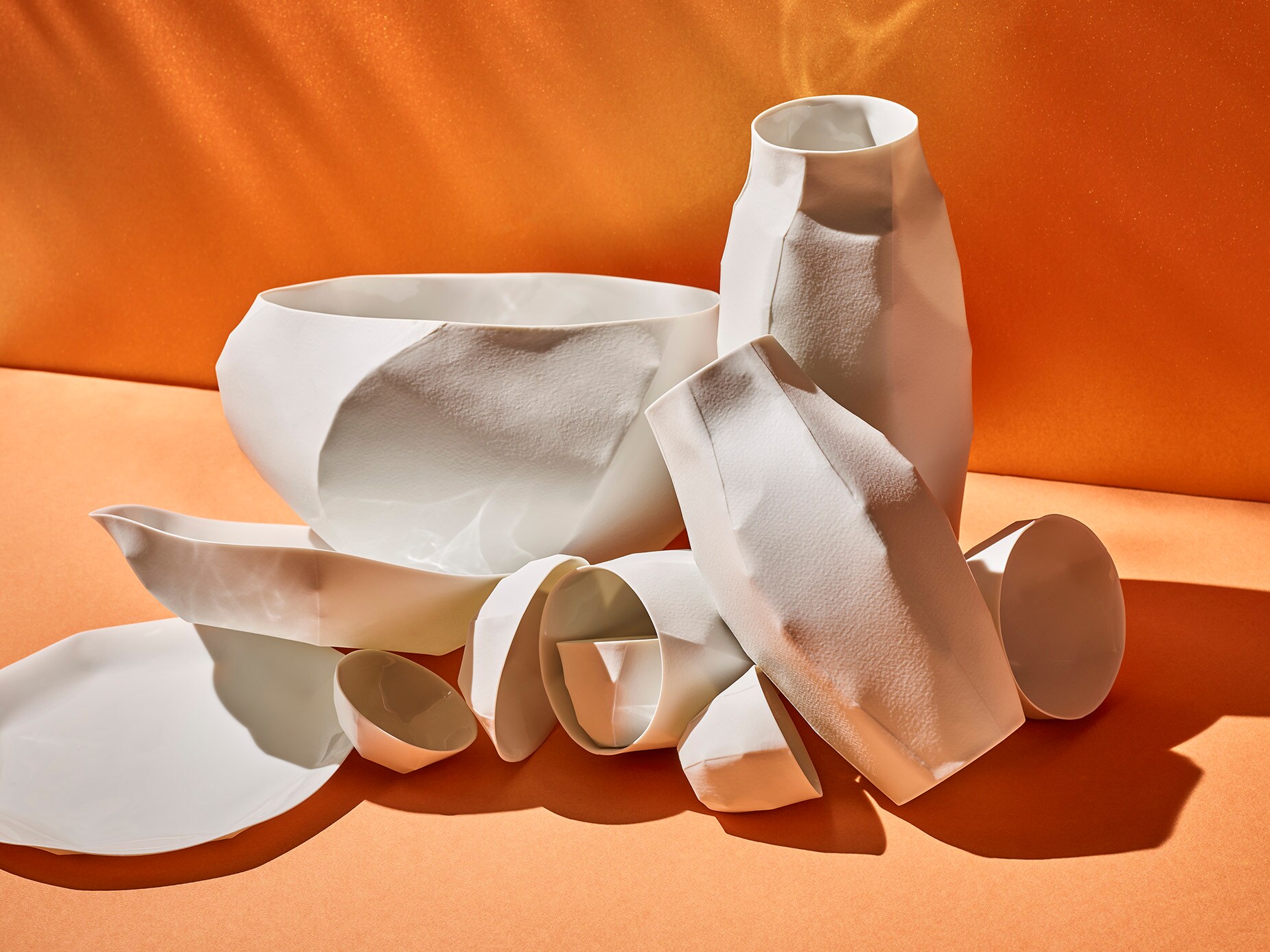 Ein Stillleben aus weißem, filigranem und kunstvollem Porzellan auf orangem Hintergrund