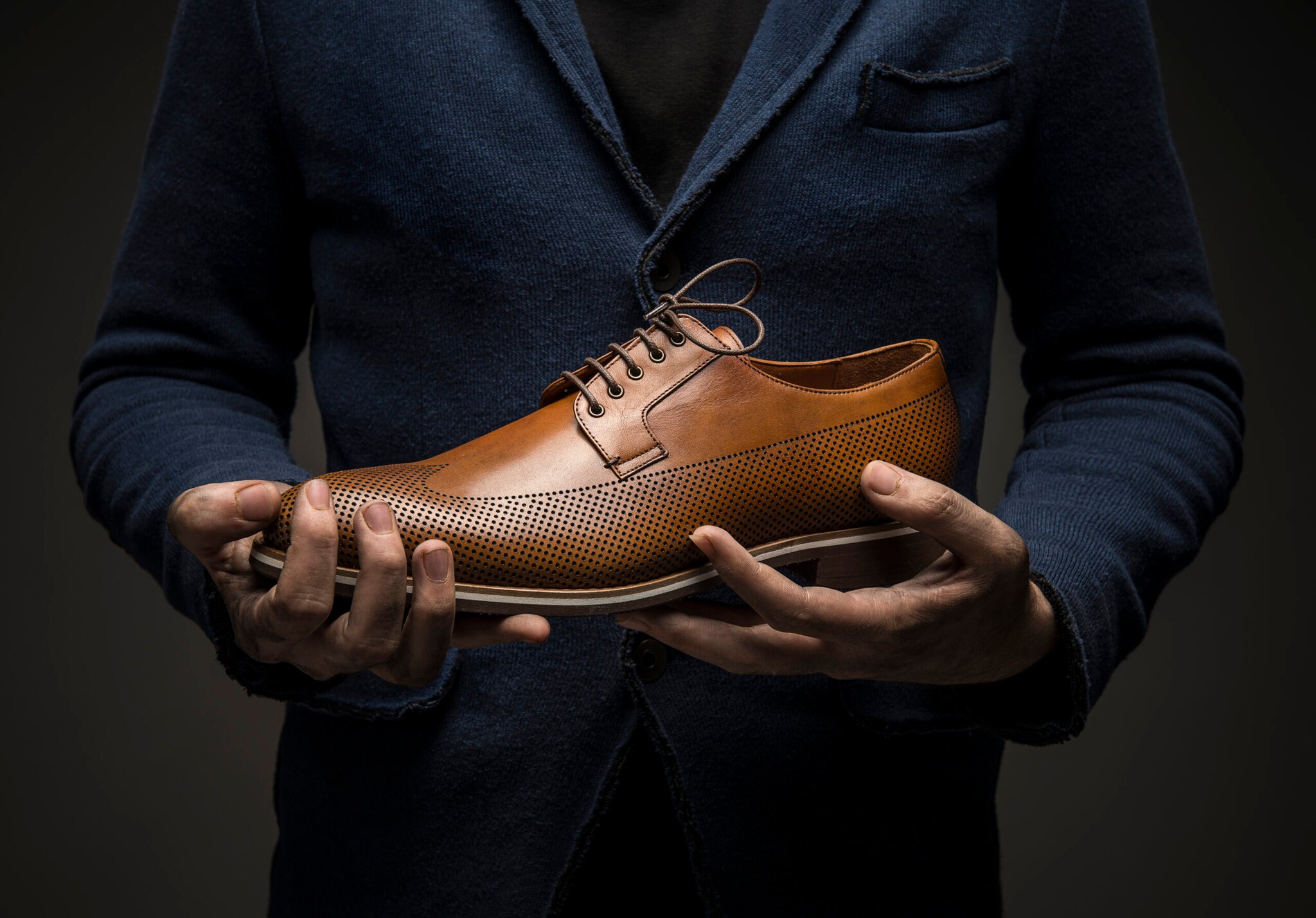 Ein Mann im dunklen Anzug hält einen eleganten Lederschuh Ein Mann im dunklen Anzug hält einen eleganten Lederschuh