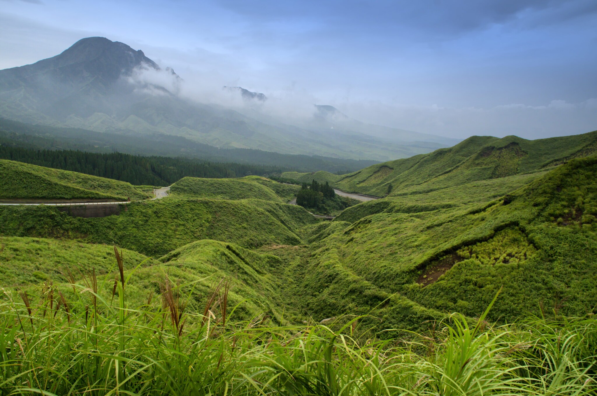 Gebirgige, grüne Landschaft mit einem Vulkan im Hintergrund