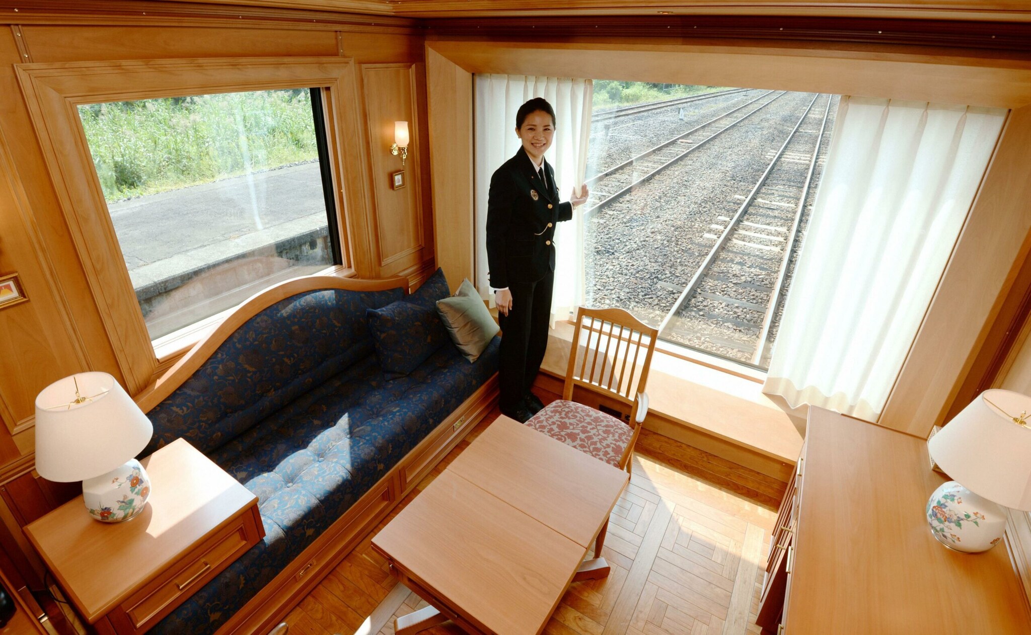 Eine Frau in Uniform steht an einem Panoramafenster in einer Suite mit Holzverkleidungen in einem Abteil am Ende des Zuges