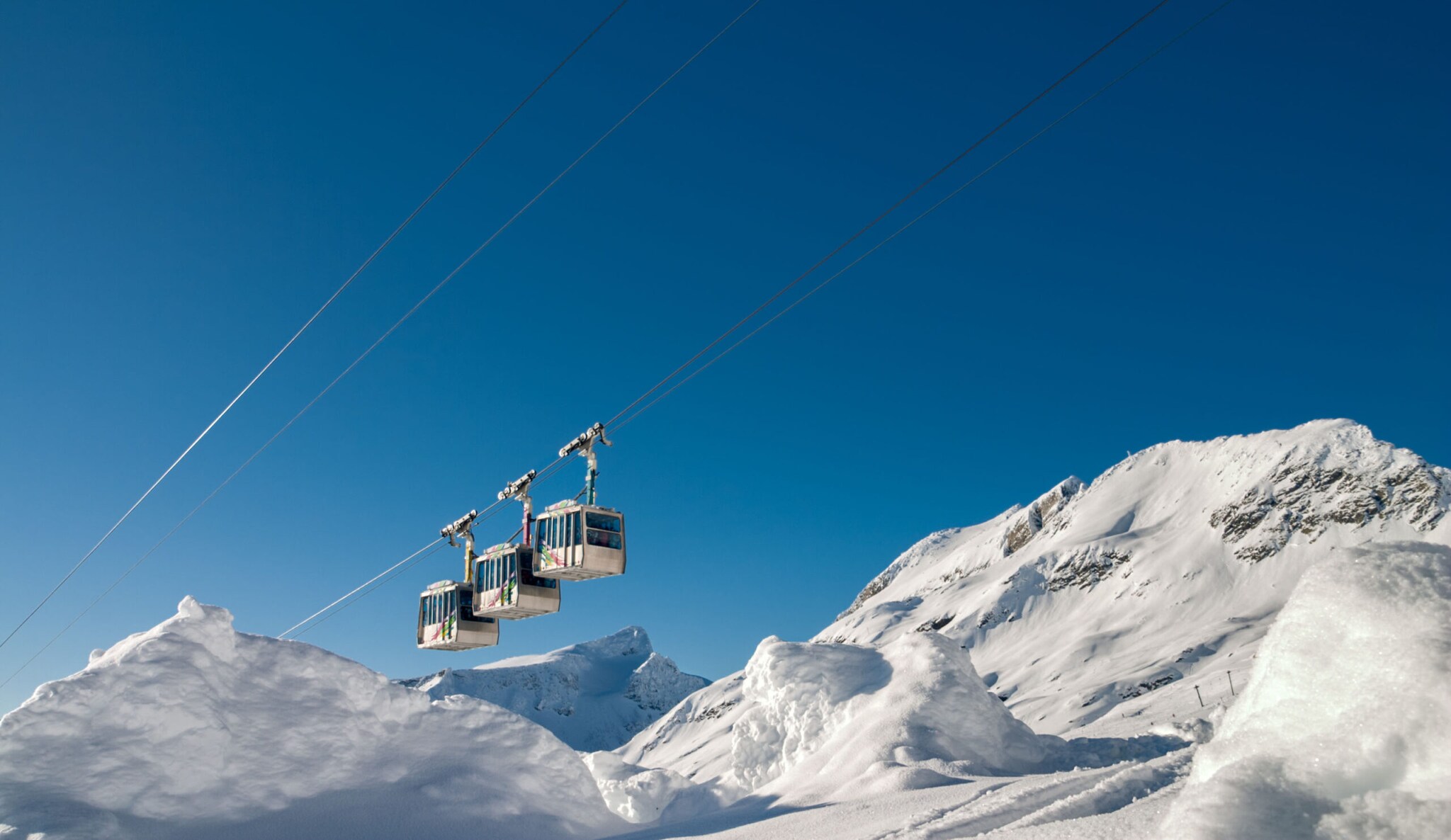 Eine Seilbahn vor blauem Himmel und schneebedeckten Bergen