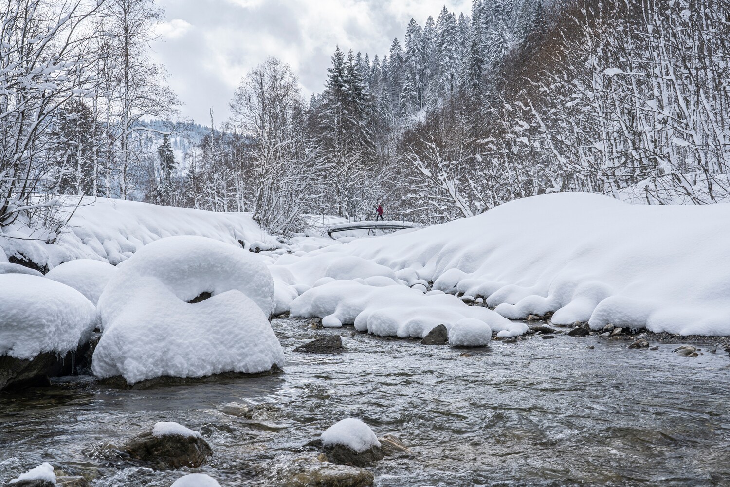 Eine Person spaziert in einer Winterlandschaft über einen schneebedeckten Fluss