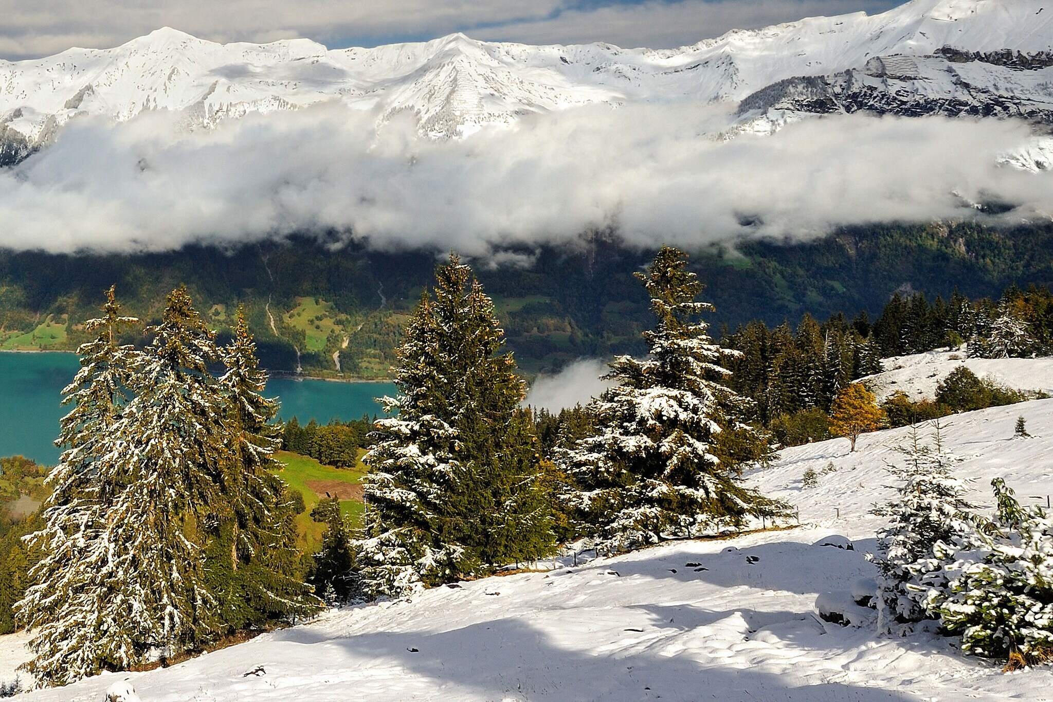 Schneebedeckte Berge, ein Bergsee und tiefhängende Wolken