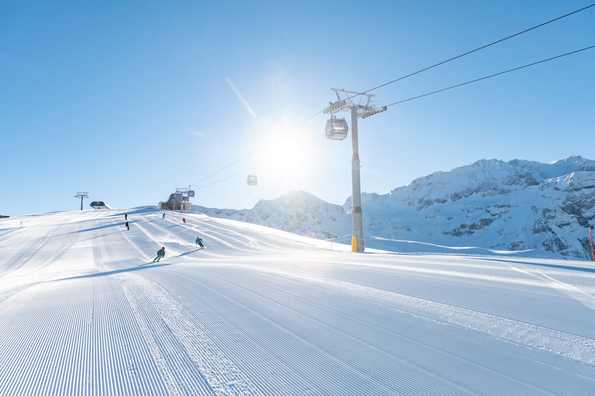 Eine präparierte Skipiste im Sonnenschein, darüber eine Gondelbahn Eine präparierte Skipiste im Sonnenschein, darüber eine Gondelbahn