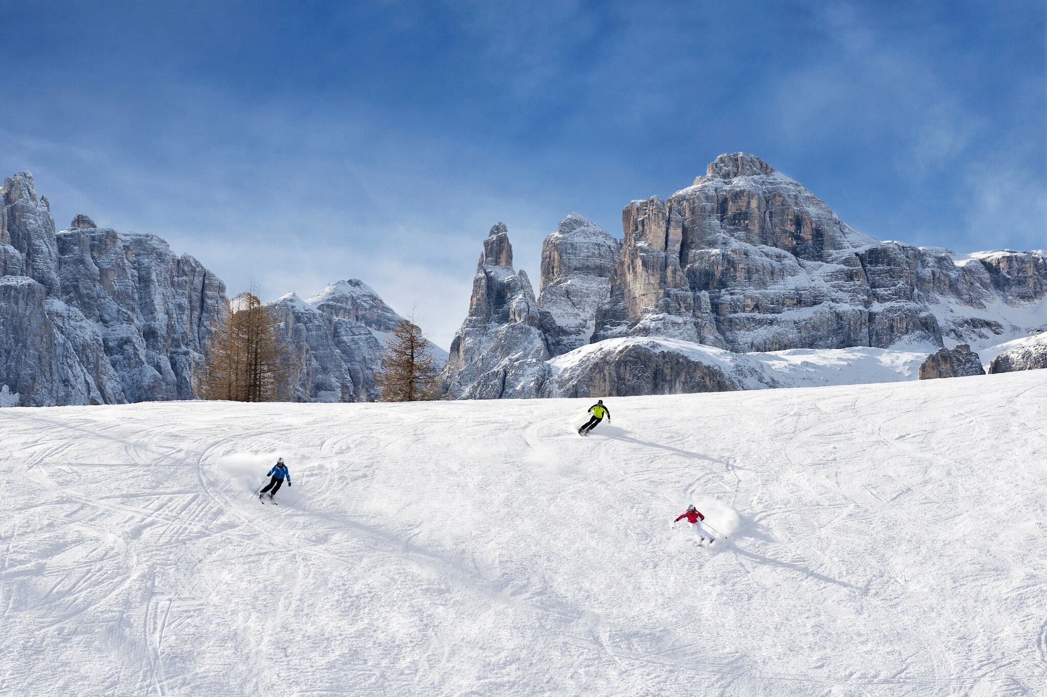 Panorama einer Skipiste mit drei Skifahrern vor markanten Felsformationen eines Bergmassivs