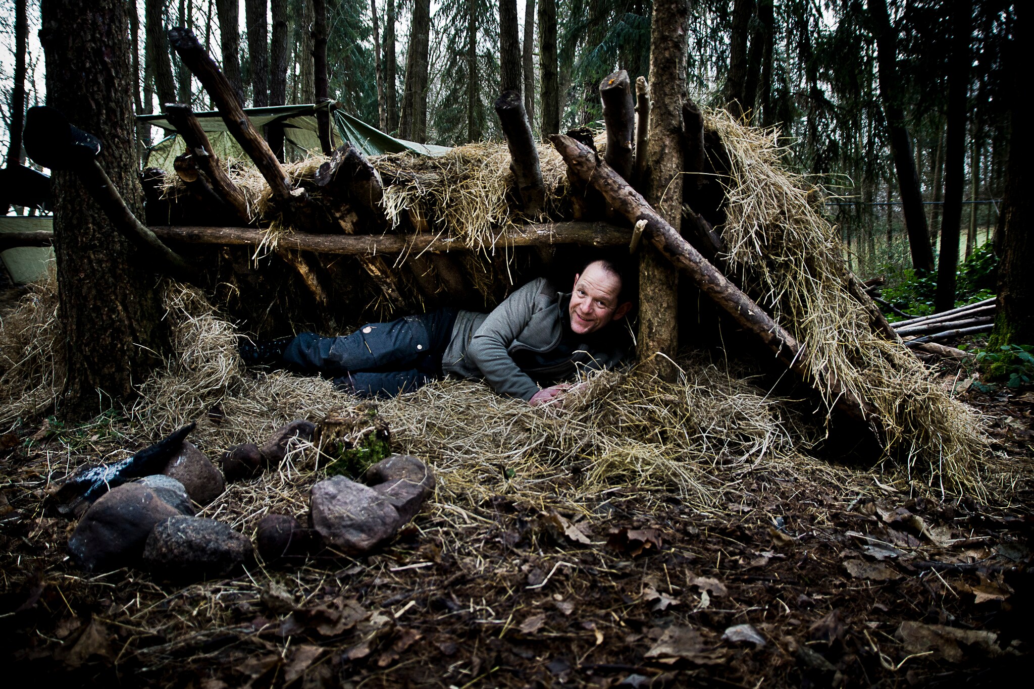 Ein Mann liegt in einem Unterschlupf aus Baumstämmen und Heu in einem Wald Ein Mann liegt in einem Unterschlupf aus Baumstämmen und Heu in einem Wald