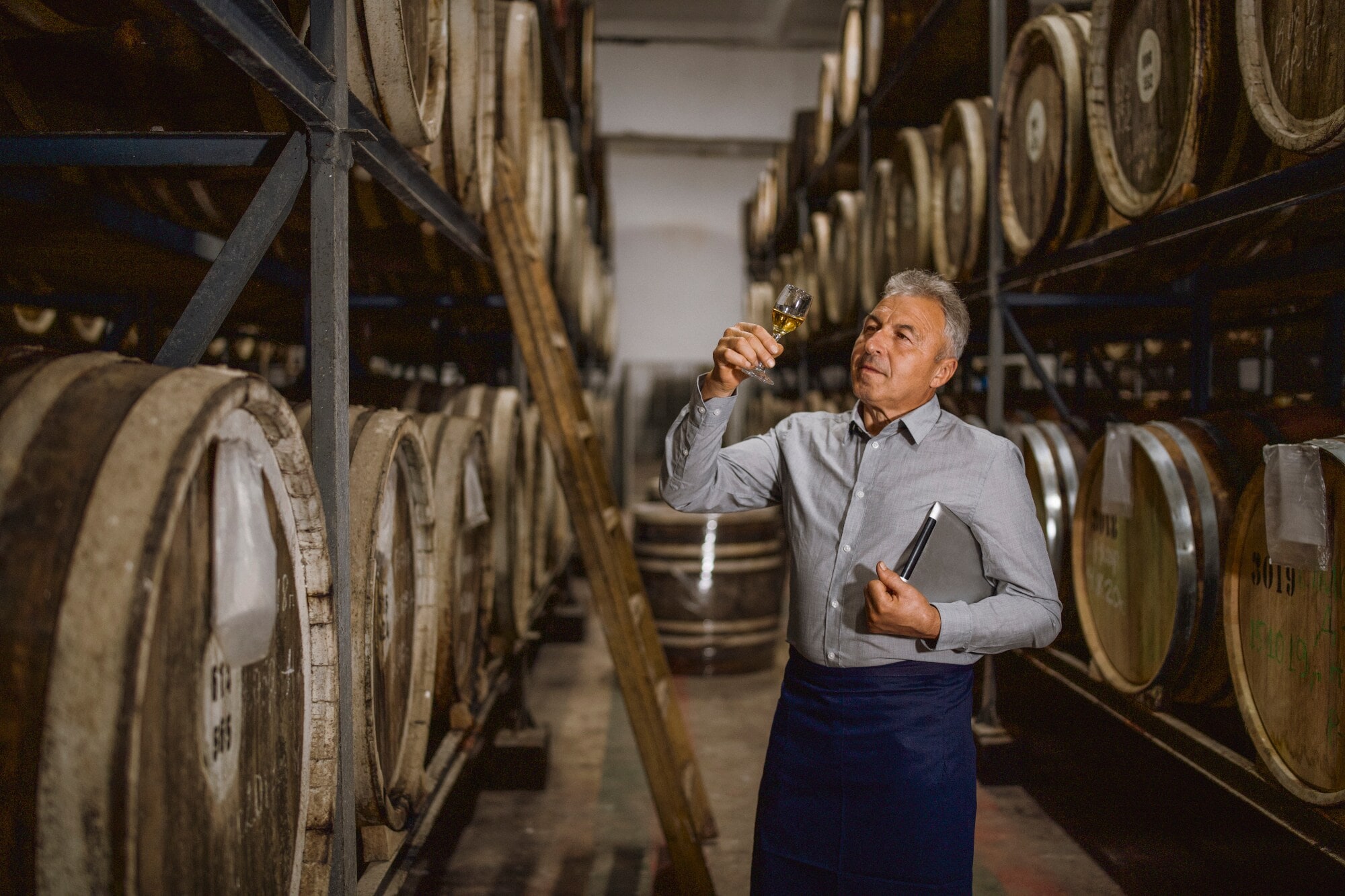 Ein Brandmeister steht in seiner Destillerie und hält ein Glas seines Whiskys prüfend gegen das Licht Ein Brandmeister steht in seiner Destillerie und hält ein Glas seines Whiskys prüfend gegen das Licht