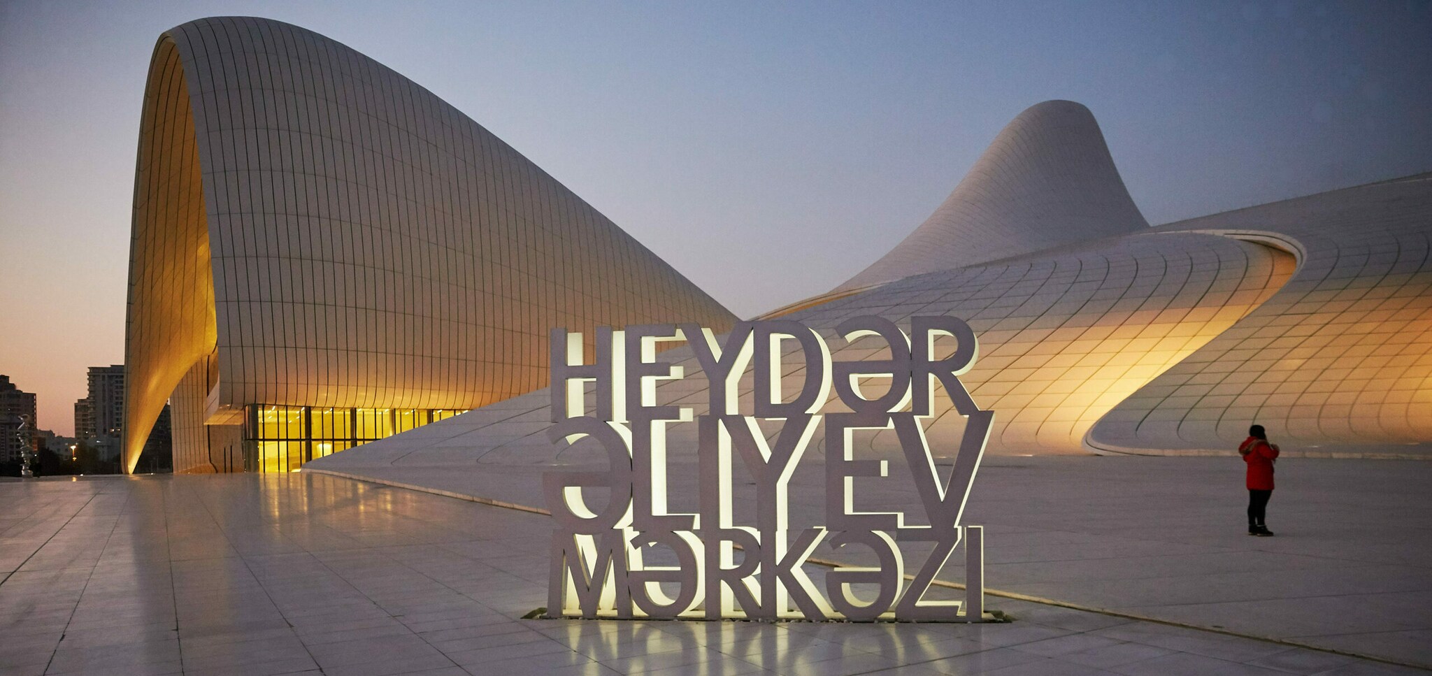 Ein Vorplatz eines geschwungenen Gebäudes, darauf ein großer Schriftzug