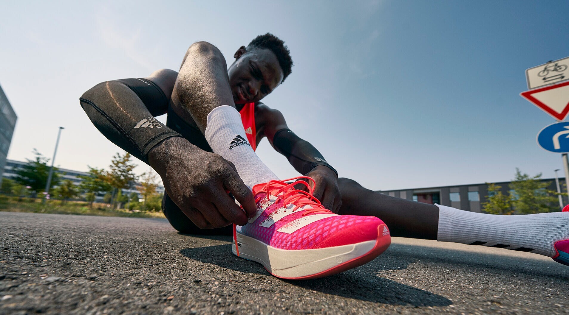 Ein athletischer Läufer sitzt auf dem Asphalt und bindet seinen Sportschuh zu