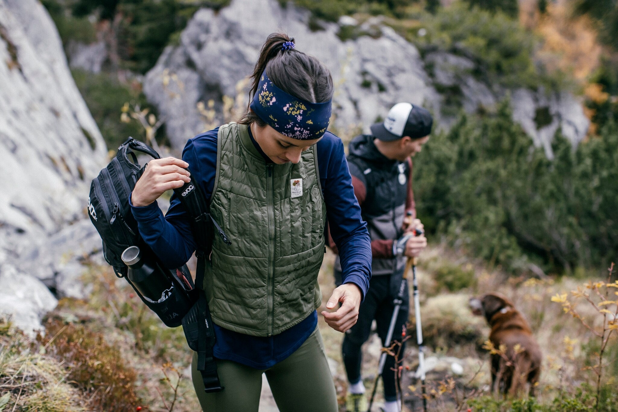 Eine Frau und ein Mann in Sportkleidung sind mit ihrem Hund in den waldreichen und herbstlichen Bergen unterwegs