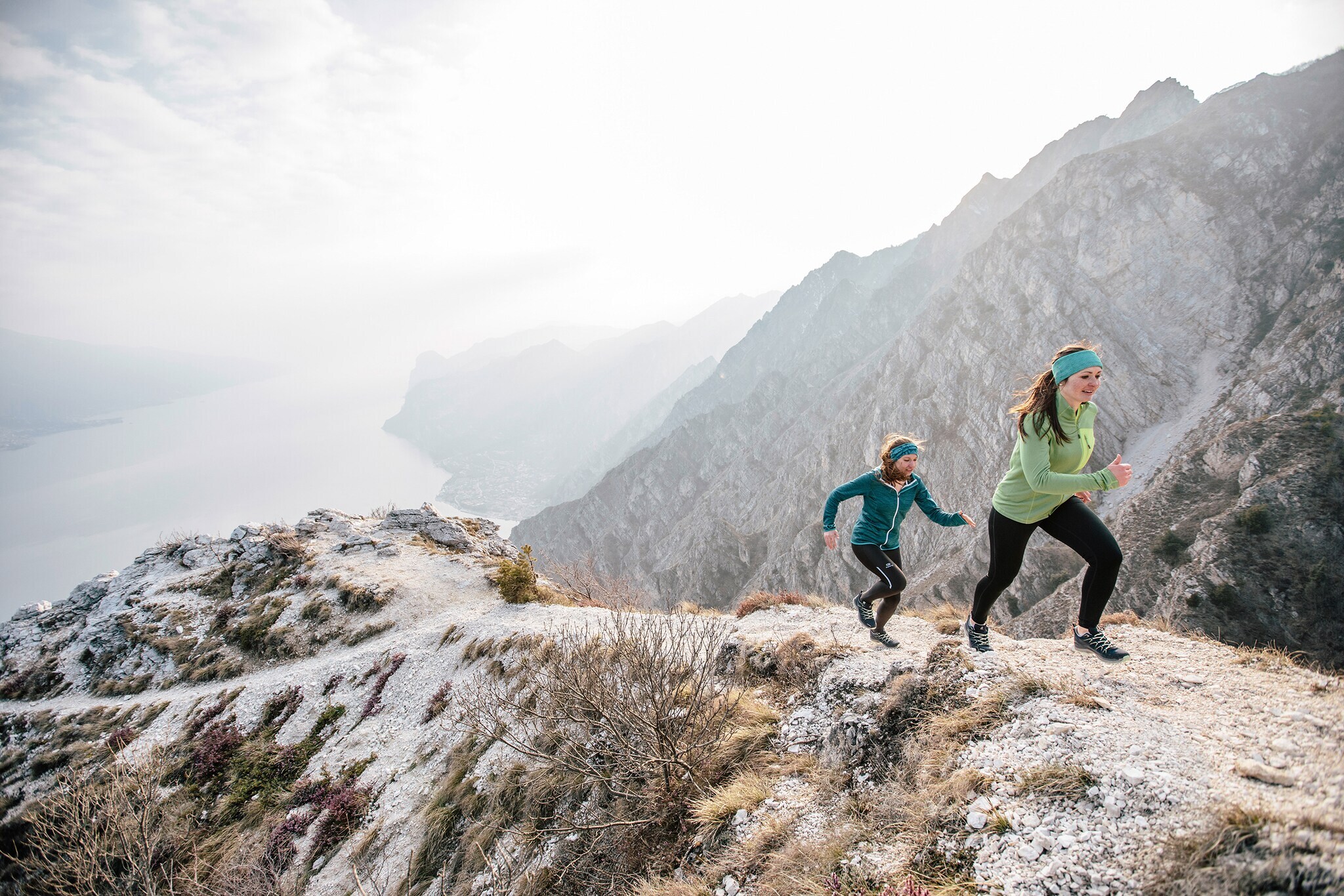 Zwei Läuferinnen sprinten bei kühler Witterung einen steilen und felsigen Fluss-Hang hinauf