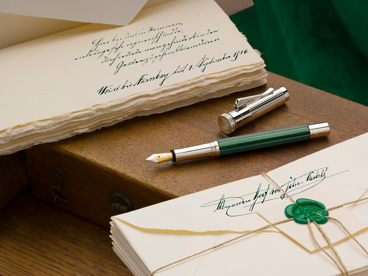 Ein grün-silberner Füllfederhalter auf hölzernem Untergrun zwischen zwei nostalgischen Briefstapeln