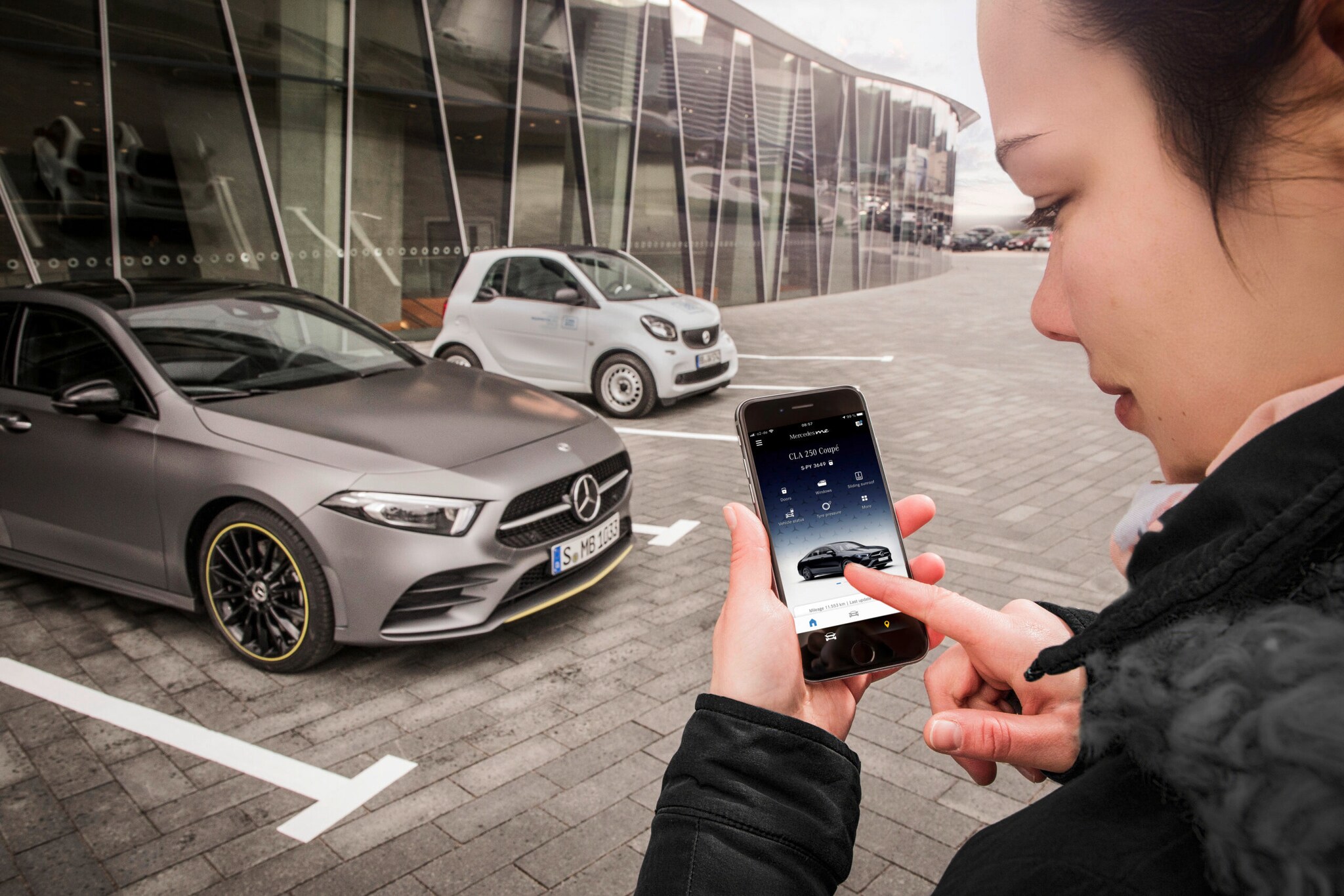 Eine Frau steht mit ihrem Smartphone vor einem Mercedes.