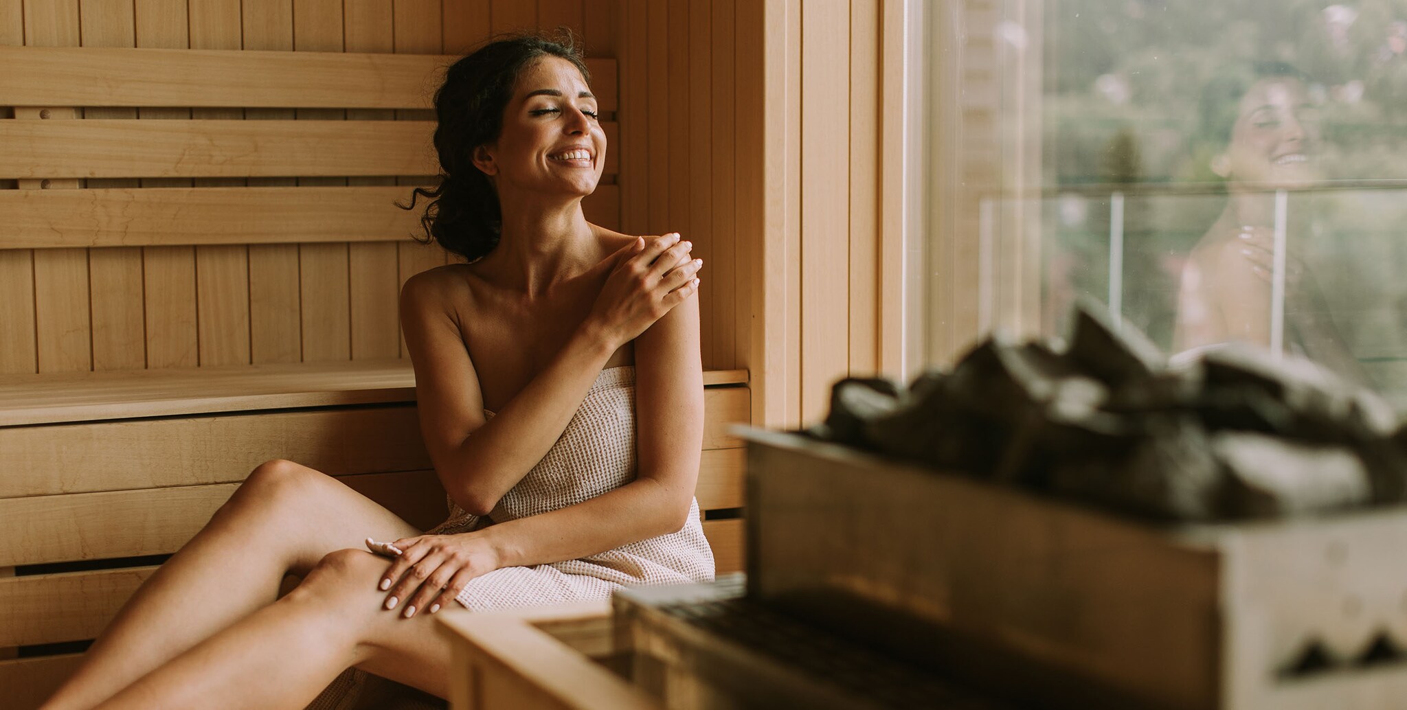 Eine lachende Frau sitzt eingewickelt in ein handtuch in einer Holzsauna.