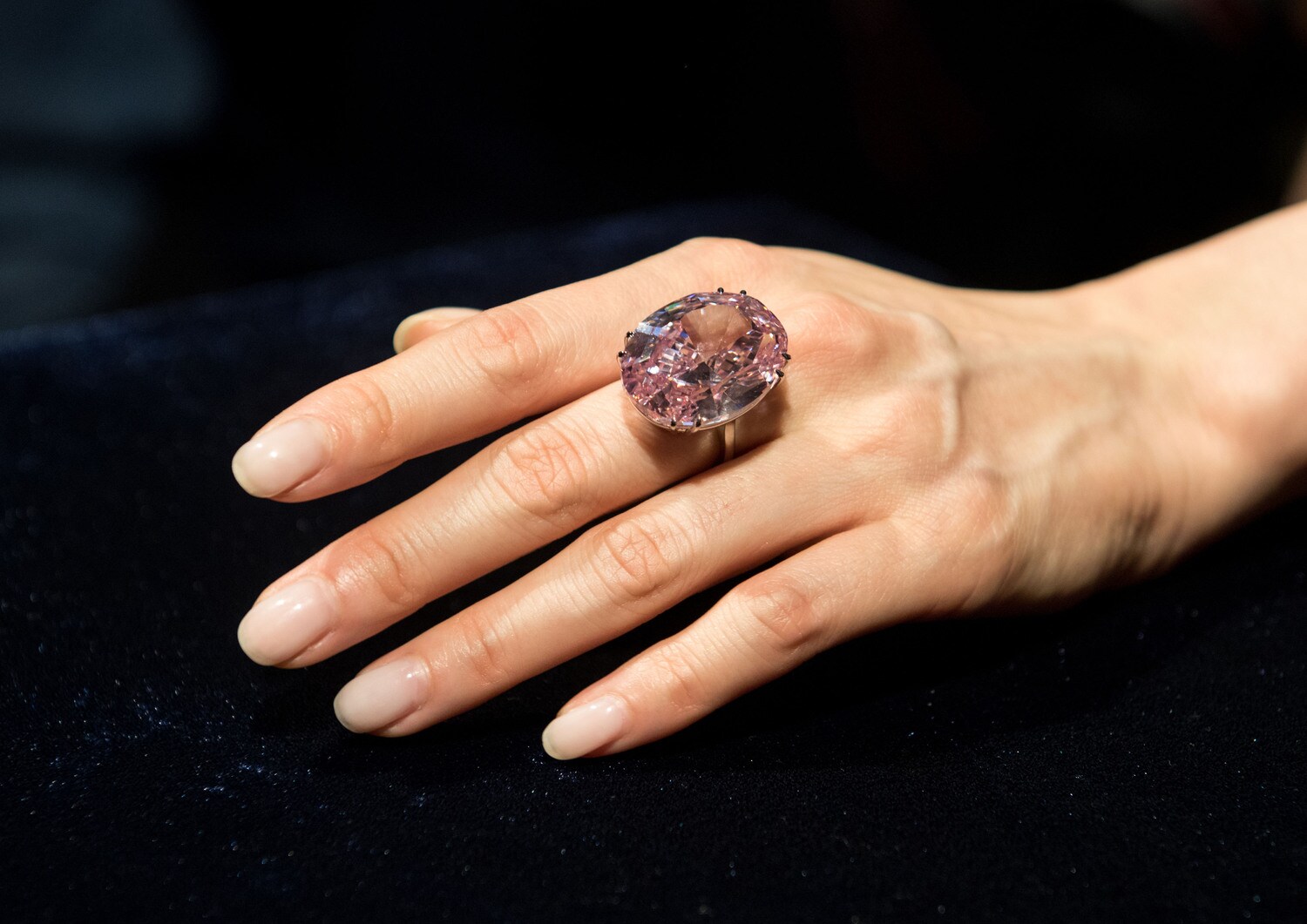 Eine weibliche Hand mit einem großen, rosafarbenen Diamantring am Mittelfinger Eine weibliche Hand mit einem großen, rosafarbenen Diamantring am Mittelfinger