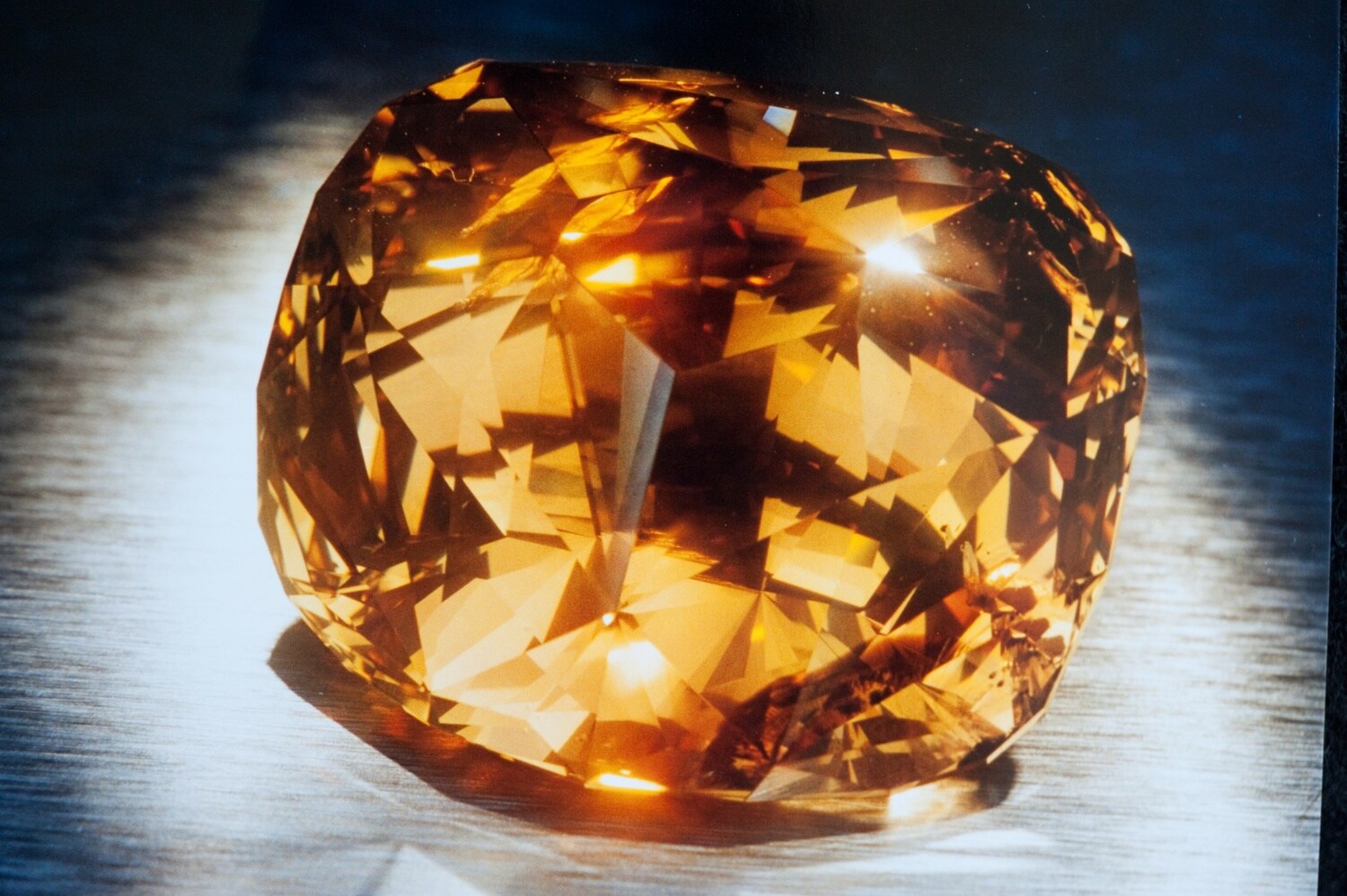 Nahaufnahme eines goldfarbenen, glitzernden Diamanten auf blauem Untergrund Nahaufnahme eines goldfarbenen, glitzernden Diamanten auf blauem Untergrund