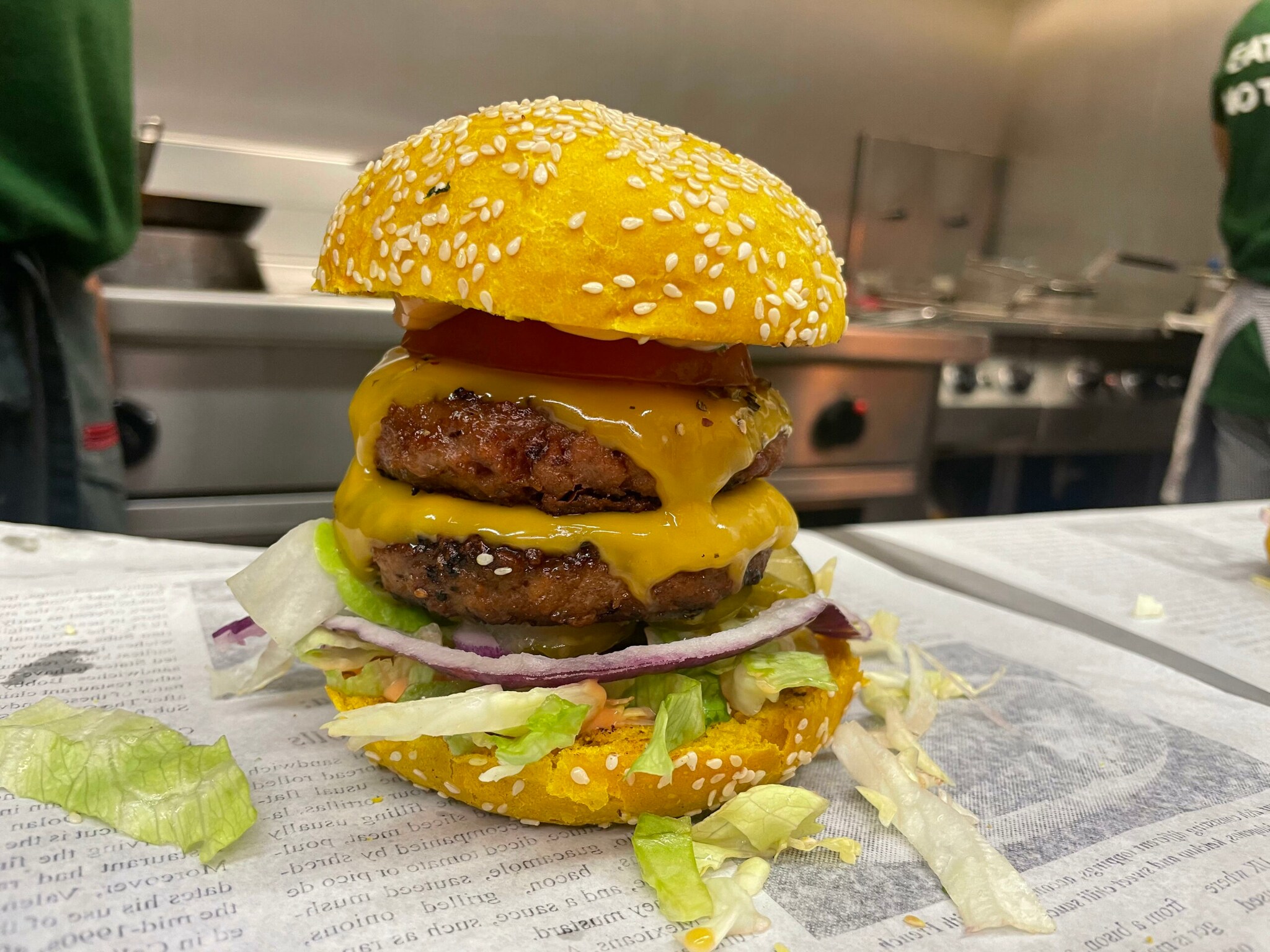 Nahaufnahme eines gestapelten, vegetarischen Cheeseburgers mit gelben Brötchenhälften in einer Küche