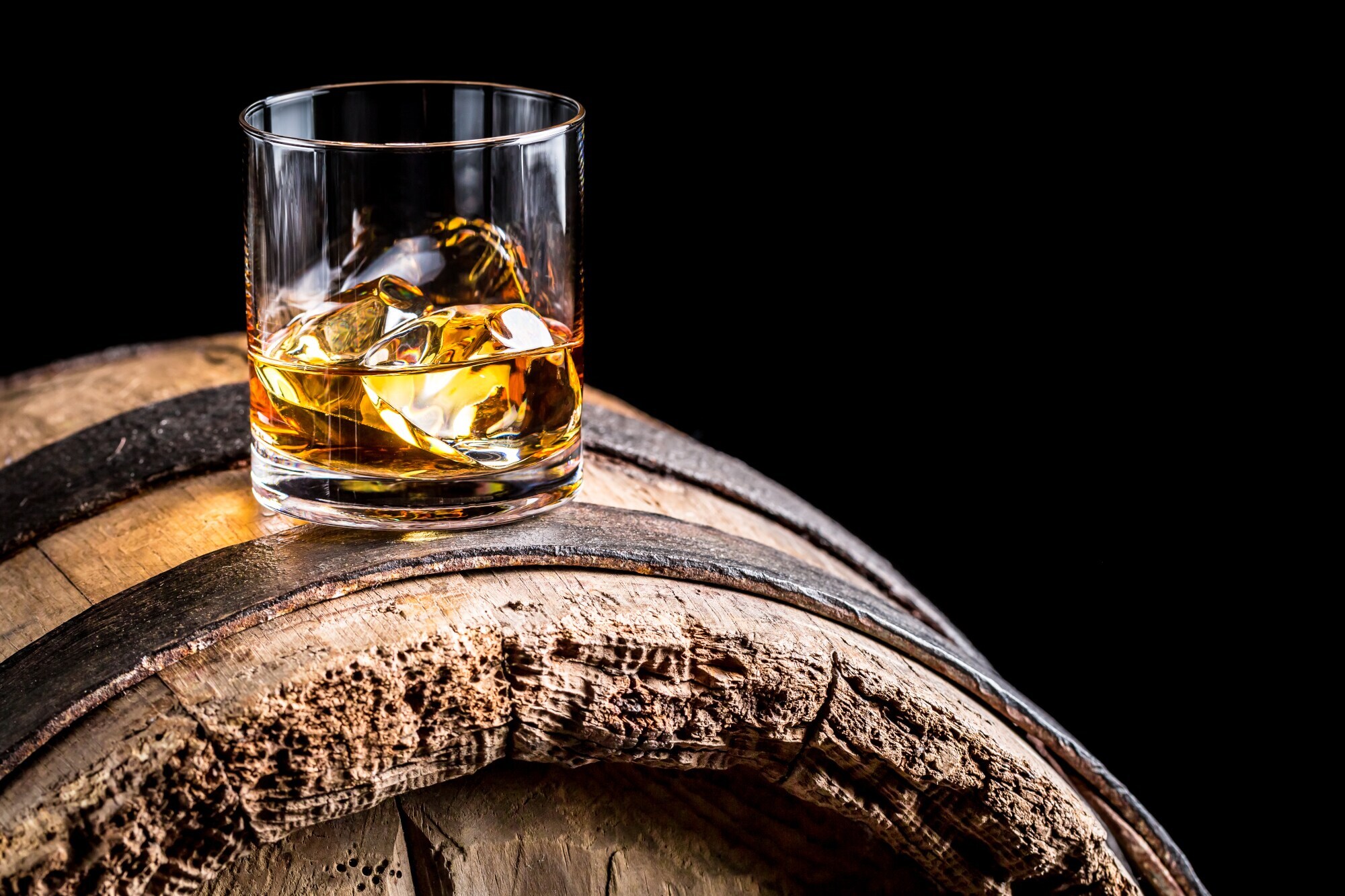 Ein Glas Whiskey mit Eiswürfeln auf einem alten hölzernen Barrel