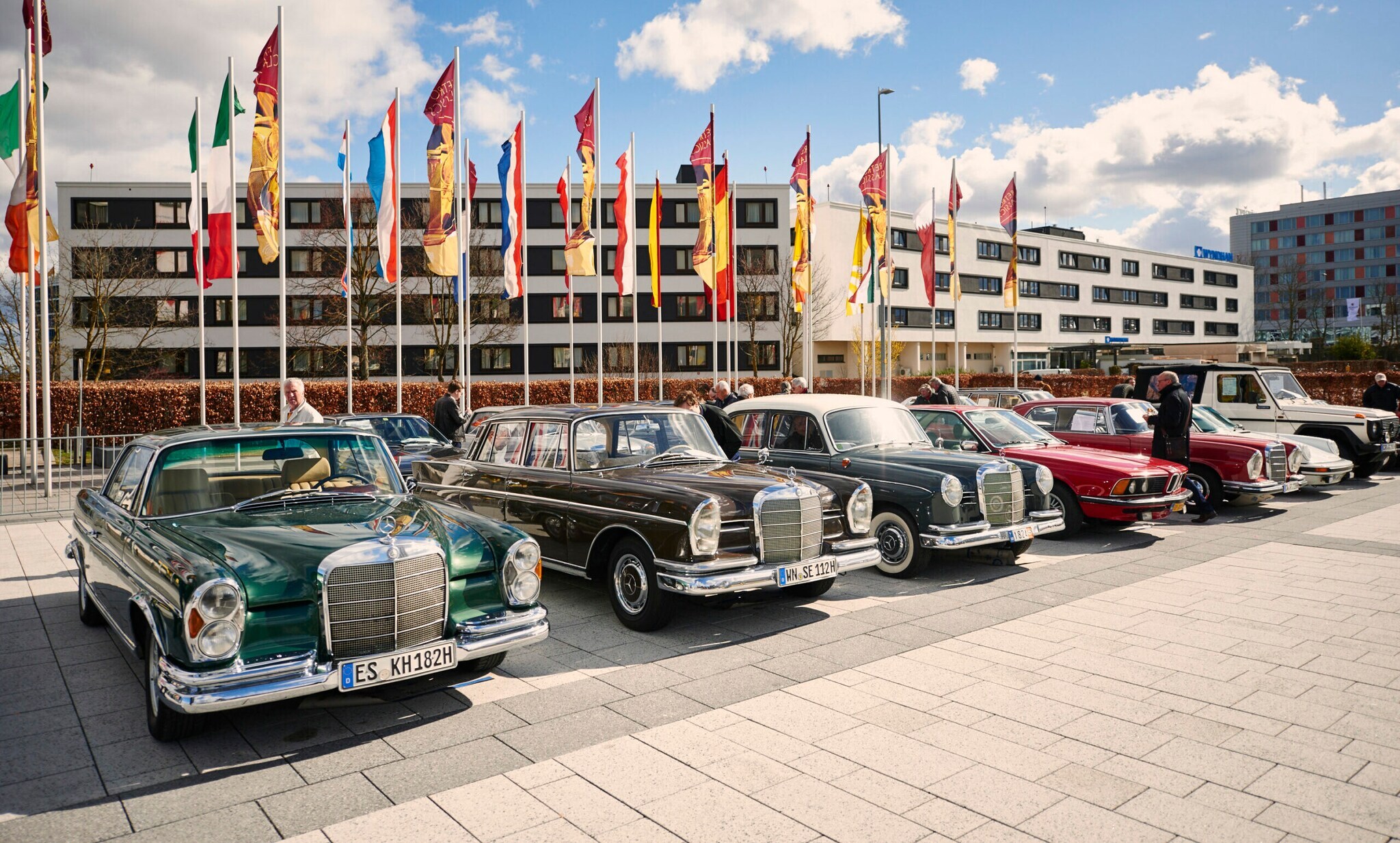 Oldtimer in einer Reihe vor einem Gebäude und Fahnen Oldtimer in einer Reihe vor einem Gebäude und Fahnen