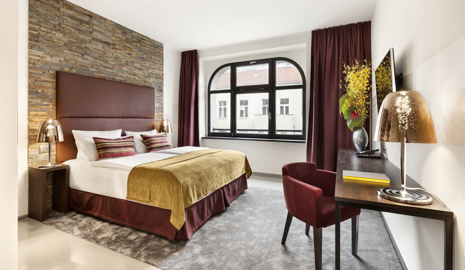 Innenansicht eines Hotelzimmers mit Doppelbett, kleinem Sessel und einem Tisch Innenansicht eines Hotelzimmers mit Doppelbett, kleinem Sessel und einem Tisch