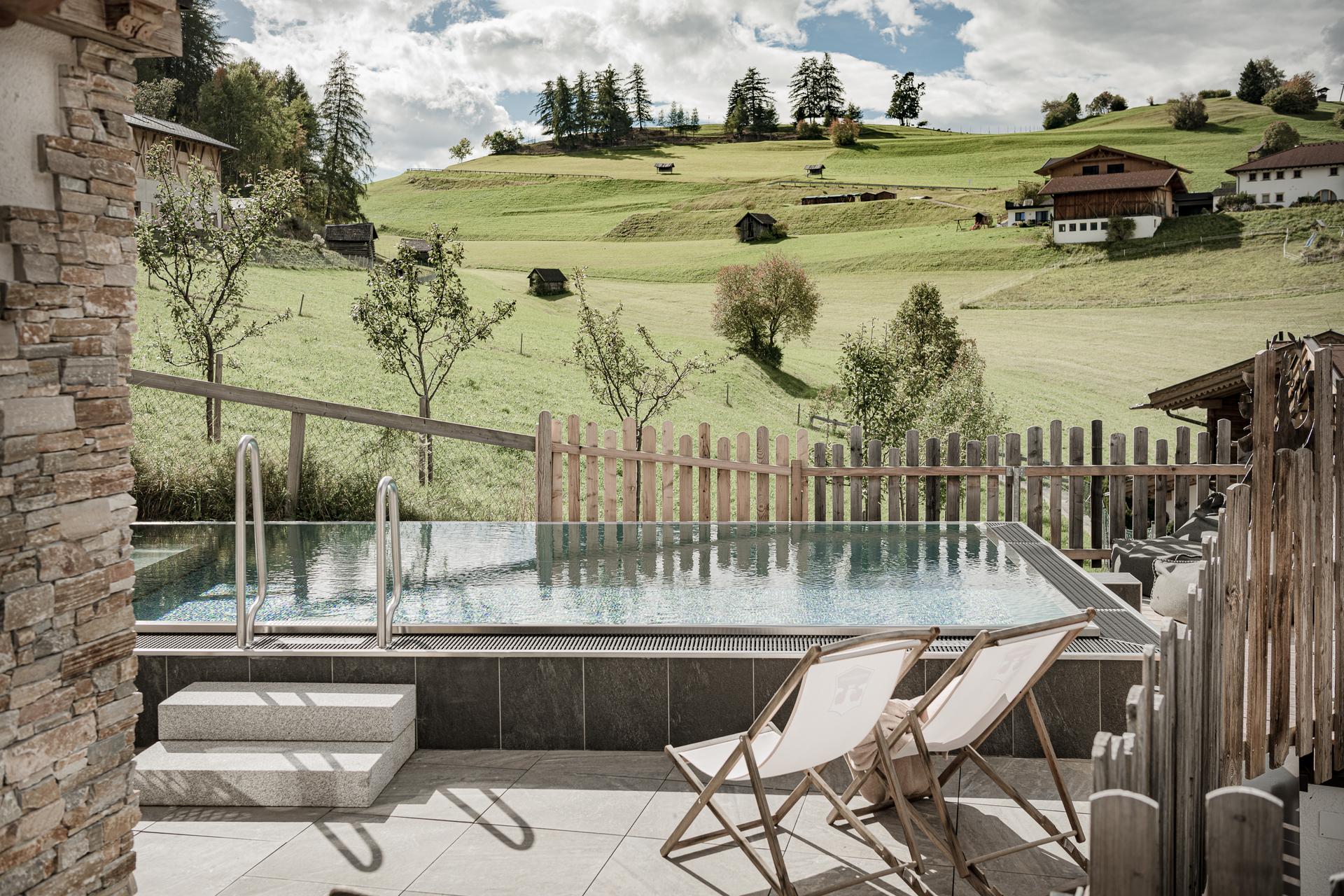 Ein Pool mit Sonnenliegen vor einer Bergkulisse bei Sonnenschein
