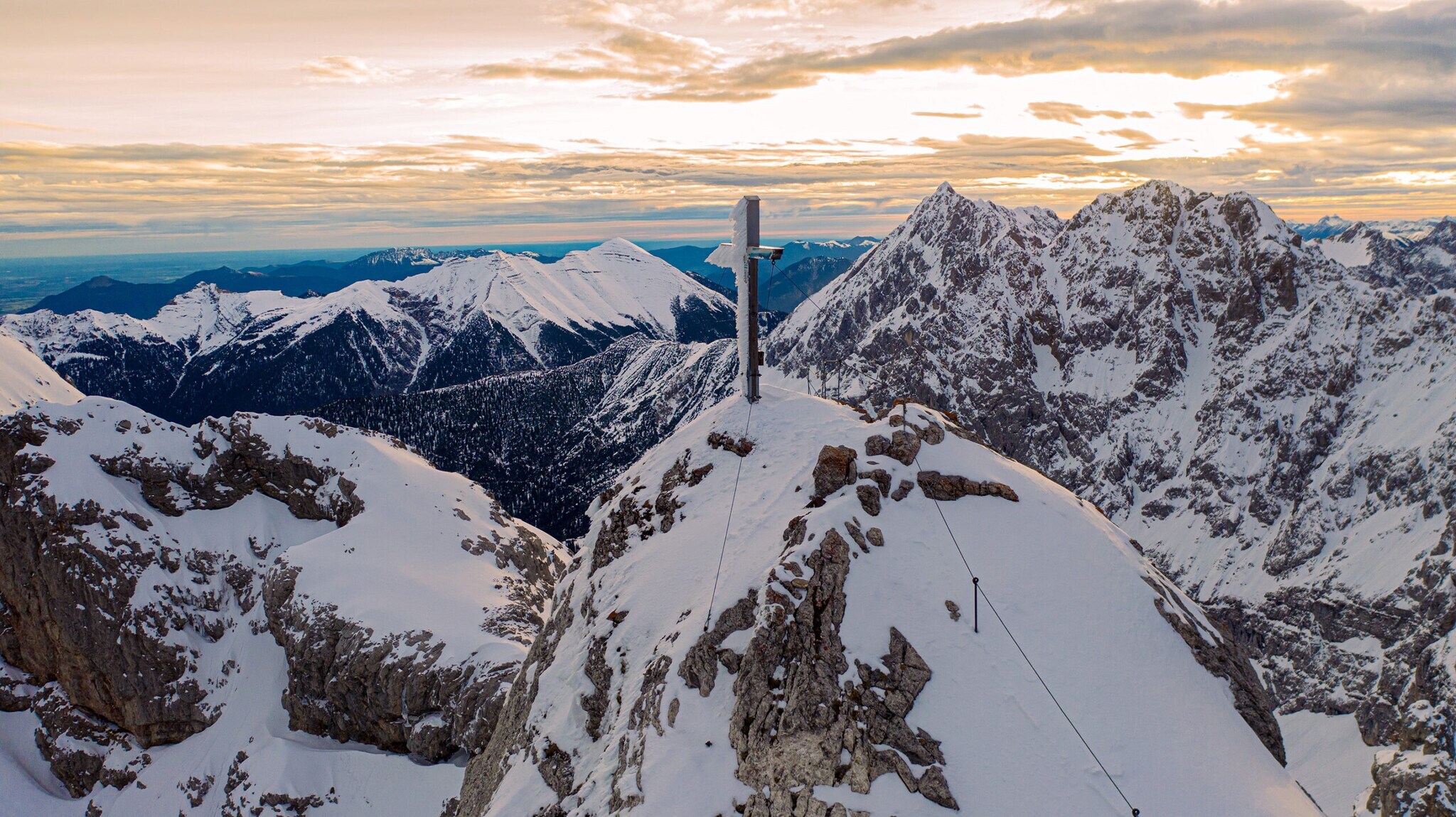 Berggipfel mit Gipfelkreuz vor schneebedeckter Bergkulisse