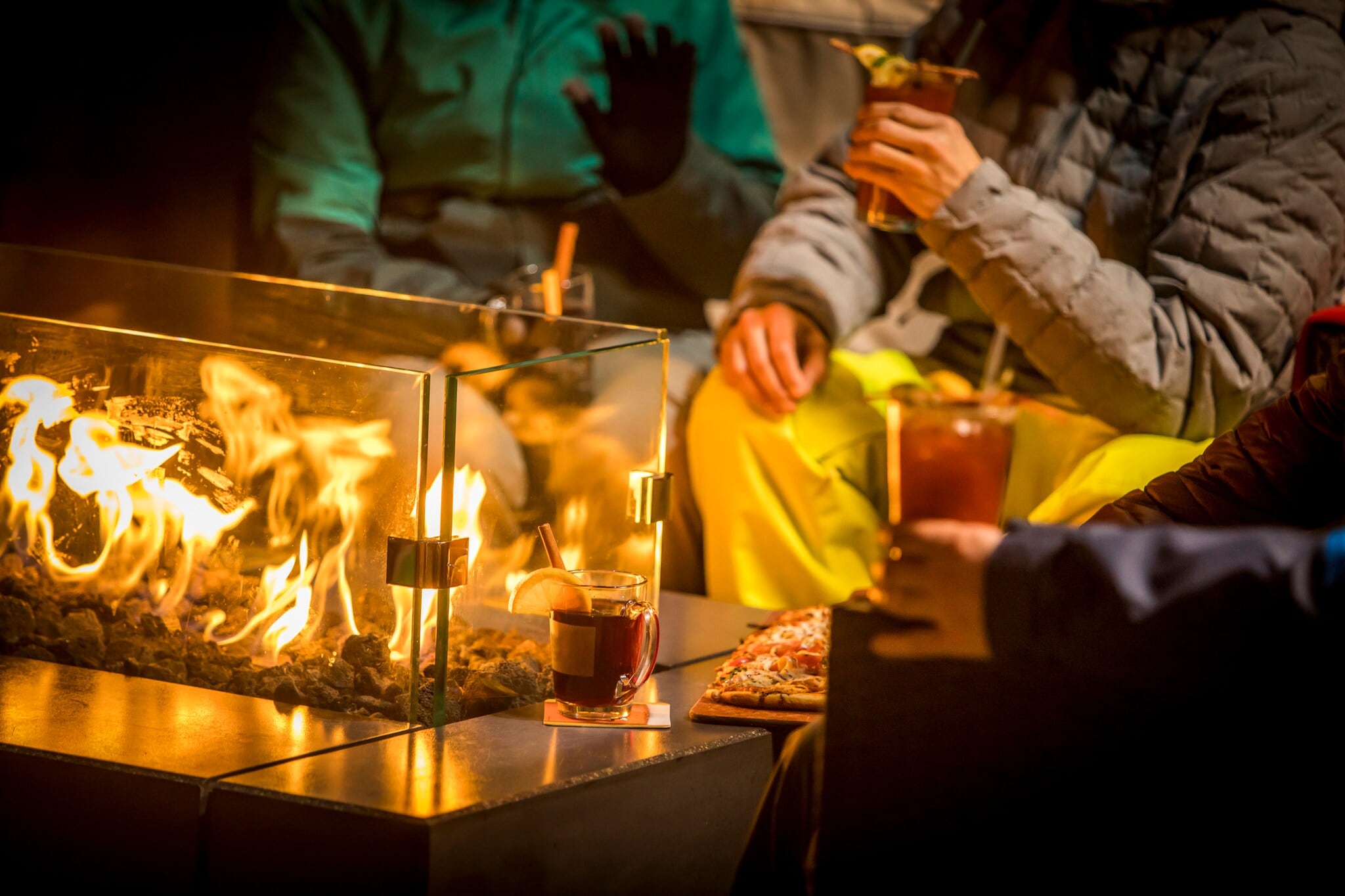 Um einen Ethanolkamin im Freien sitzen einige Menschen Um einen Ethanolkamin im Freien sitzen einige Menschen