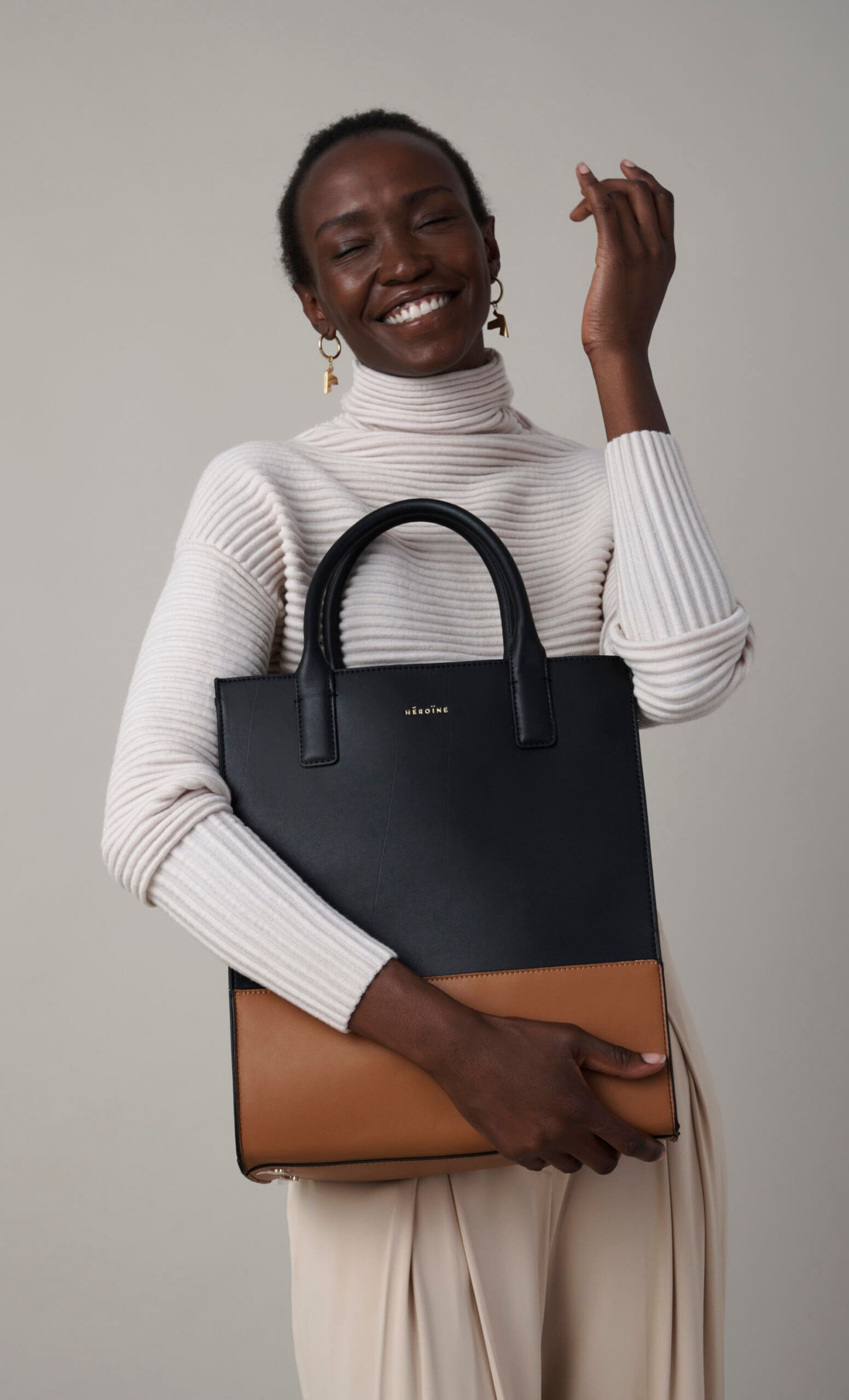 Eine Frau im hellen Pulli trägt eine Tasche aus dunklen Stoffen vor dem Oberkörper Eine Frau im hellen Pulli trägt eine Tasche aus dunklen Stoffen vor dem Oberkörper