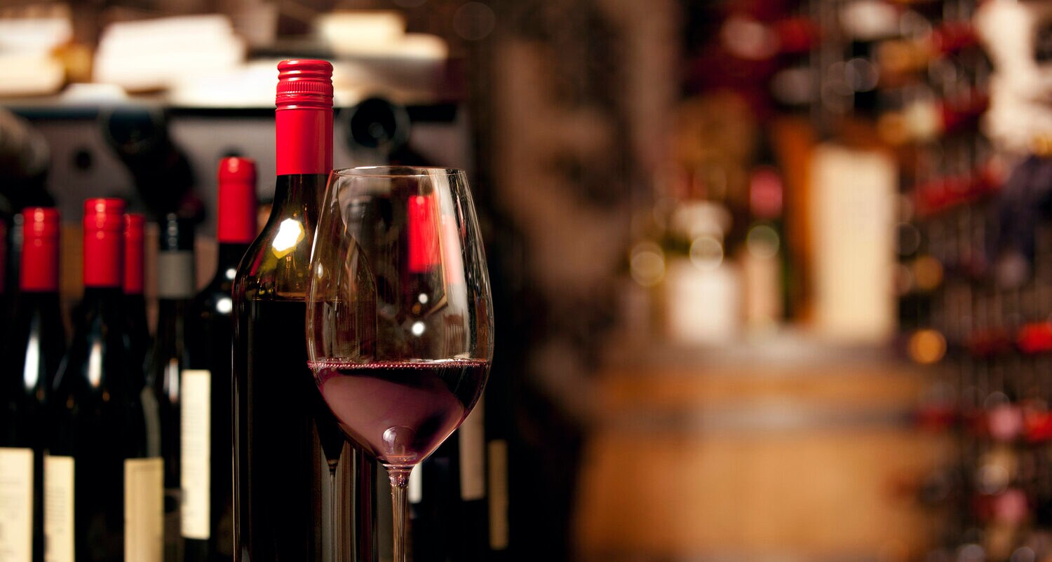 Ein Glas mit Rotwein steht auf einem Holztisch, im Hintergrund Weinfalschen Ein Glas mit Rotwein steht auf einem Holztisch, im Hintergrund Weinfalschen