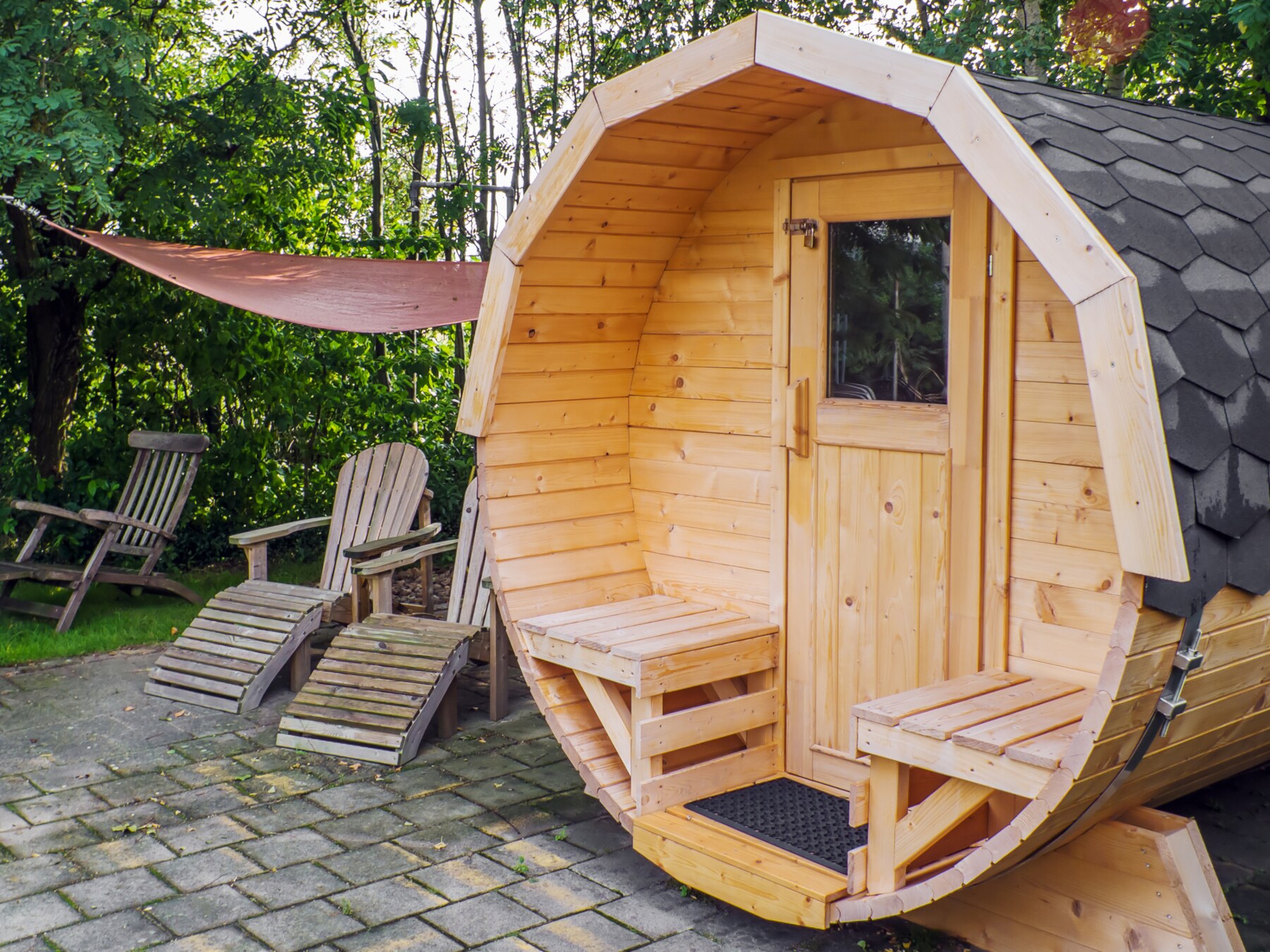Fasssauna aus Holz im Garten mit Liegestühlen Fasssauna aus Holz im Garten mit Liegestühlen