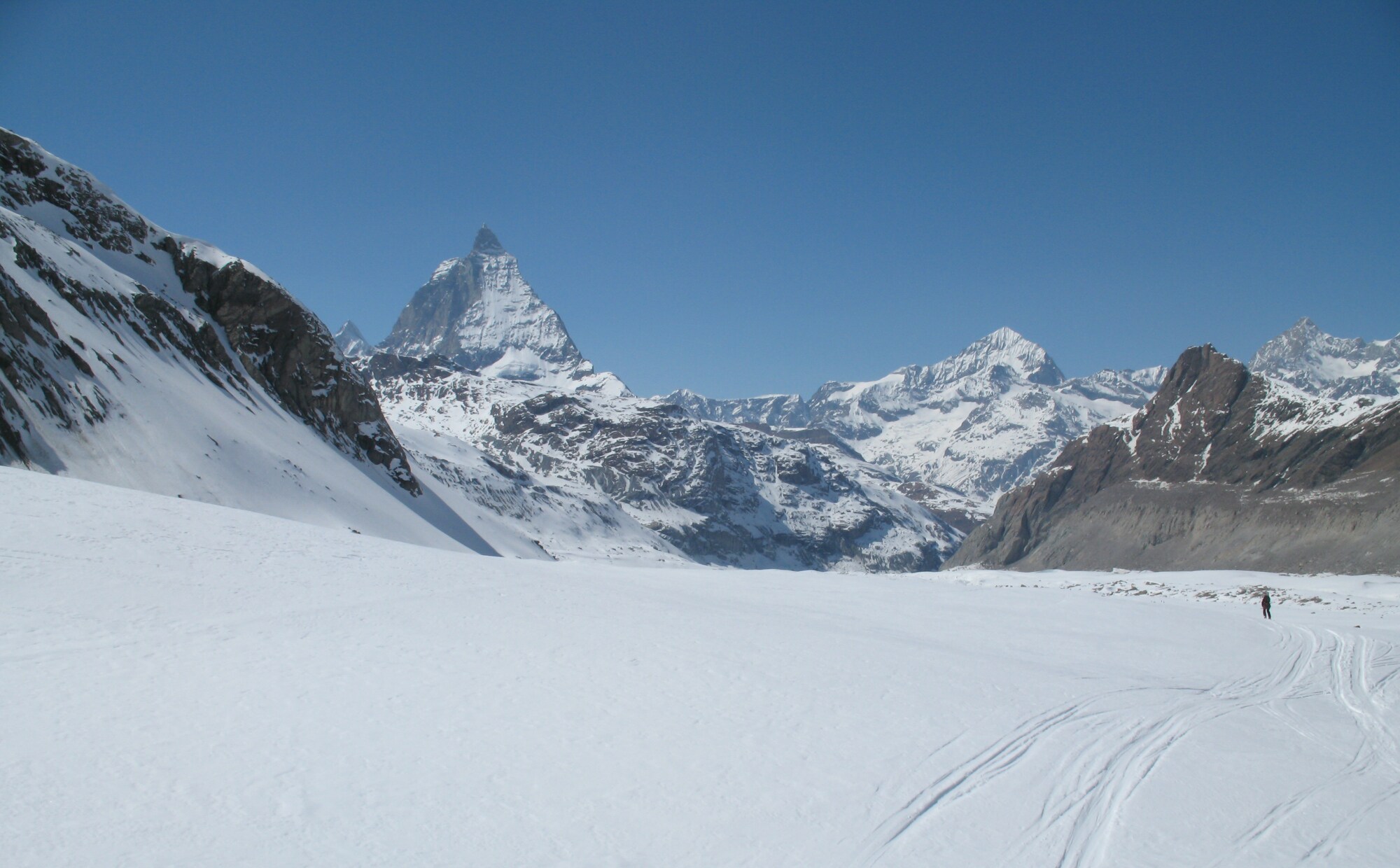 Ein Skifahrer fährt in einer weiten Ebene durch Tiefschnee, im Hintergrund verschneite Gipfel Ein Skifahrer fährt in einer weiten Ebene durch Tiefschnee, im Hintergrund verschneite Gipfel