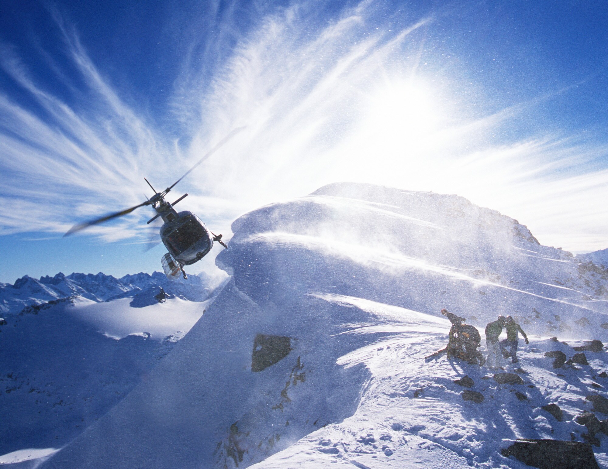 Ein Hubschrauber an einem verschneiten Berggipfel mit einer Personengruppe mit Snowboards