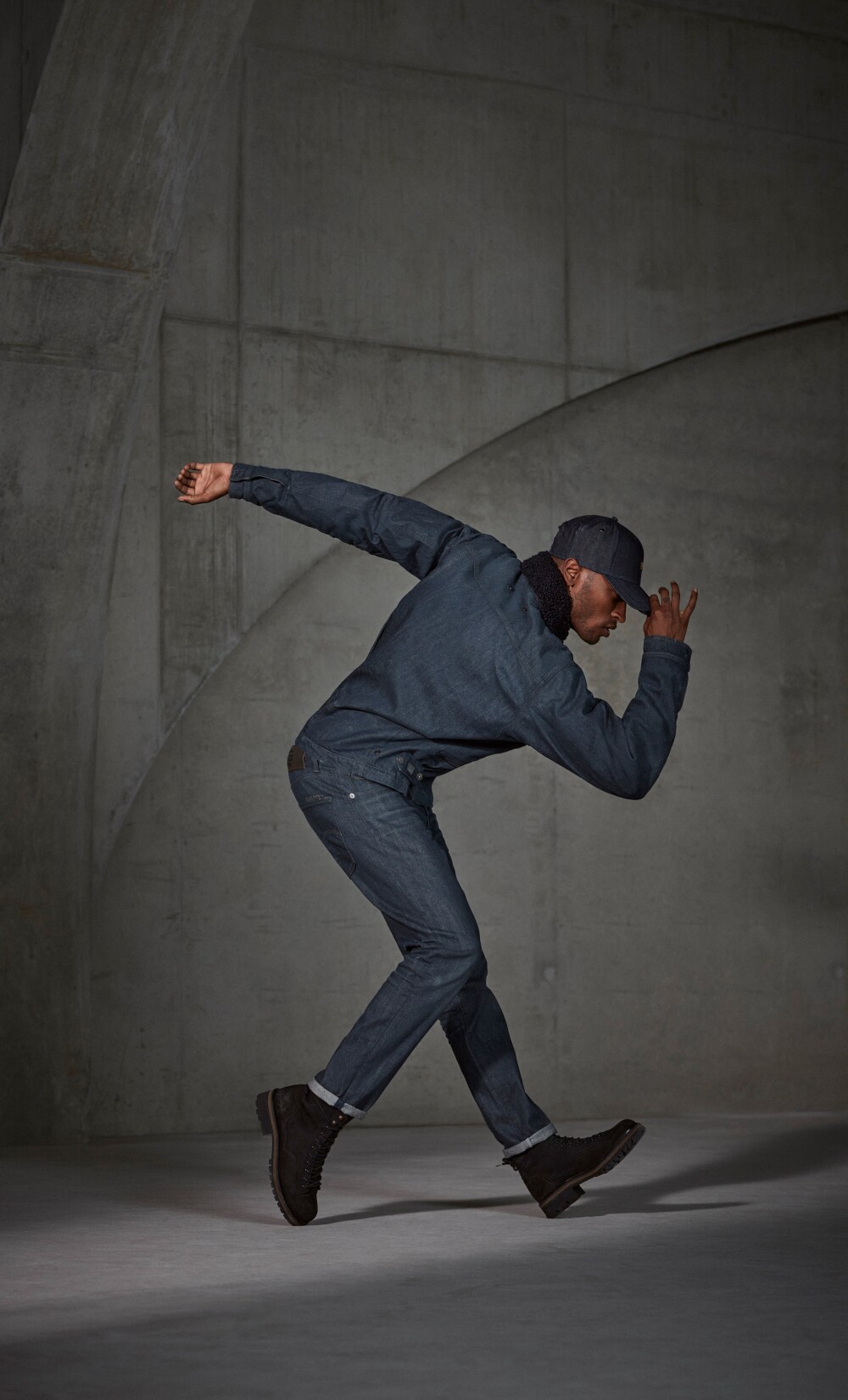 Ein Mann posiert in Jeanshose und Jeansjacke vor Betonwand Ein Mann posiert in Jeanshose und Jeansjacke vor Betonwand