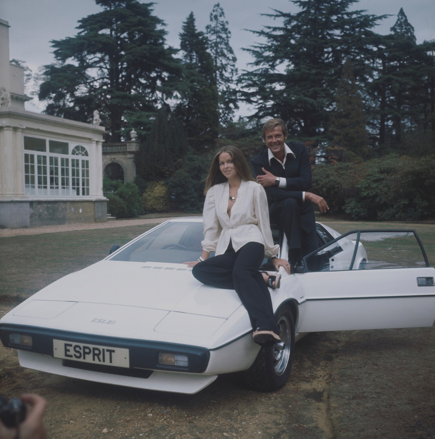 Barbara Bach und Roger Moore posieren mit einem weißen Lotus Esprit S1.