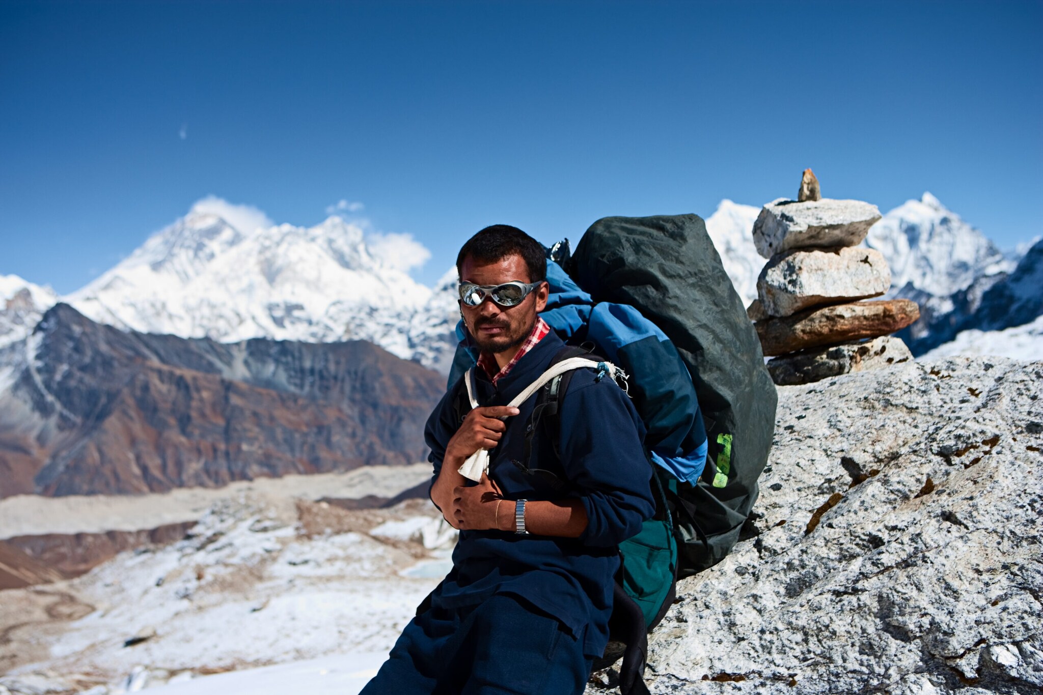 Ein Sherpa mit Rucksack lehnt an einem Felsen, im Hintergrund Berge Ein Sherpa mit Rucksack lehnt an einem Felsen, im Hintergrund Berge