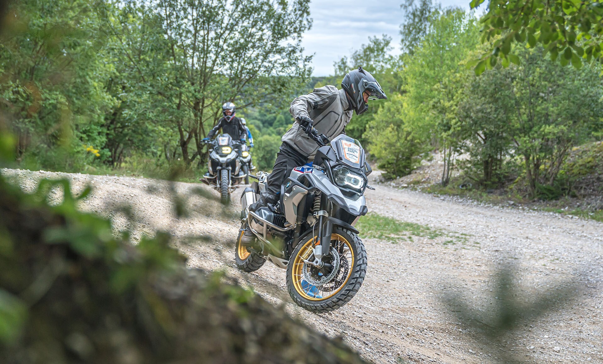 Zwei Reiseenduros der Marke BMW fahren hintereinander über eine bewaldete Schotterstrecke. Zwei Reiseenduros der Marke BMW fahren hintereinander über eine bewaldete Schotterstrecke.