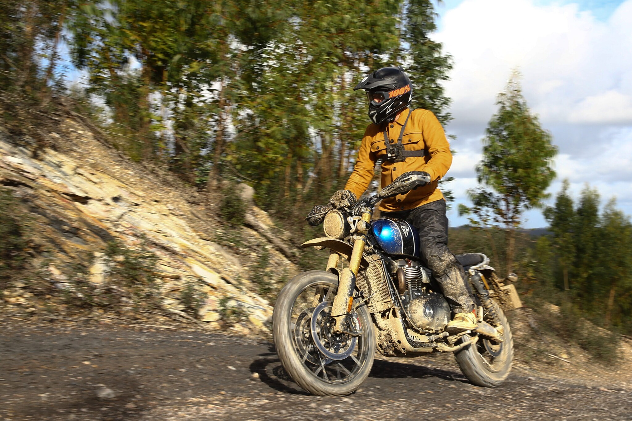 Ein Motorradfahrer fährt auf einer blauen Triumph Scrambler stehend einen Hang hinauf.