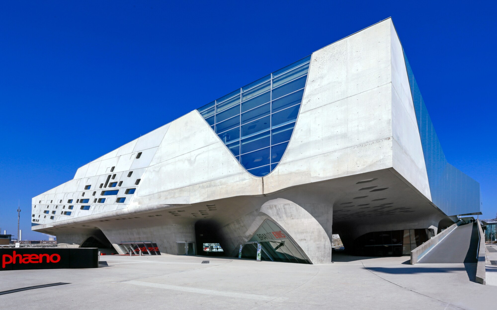 Ein großes, modernes und freistehendes Gebäude aus Beton und Glas mit Vorplatz