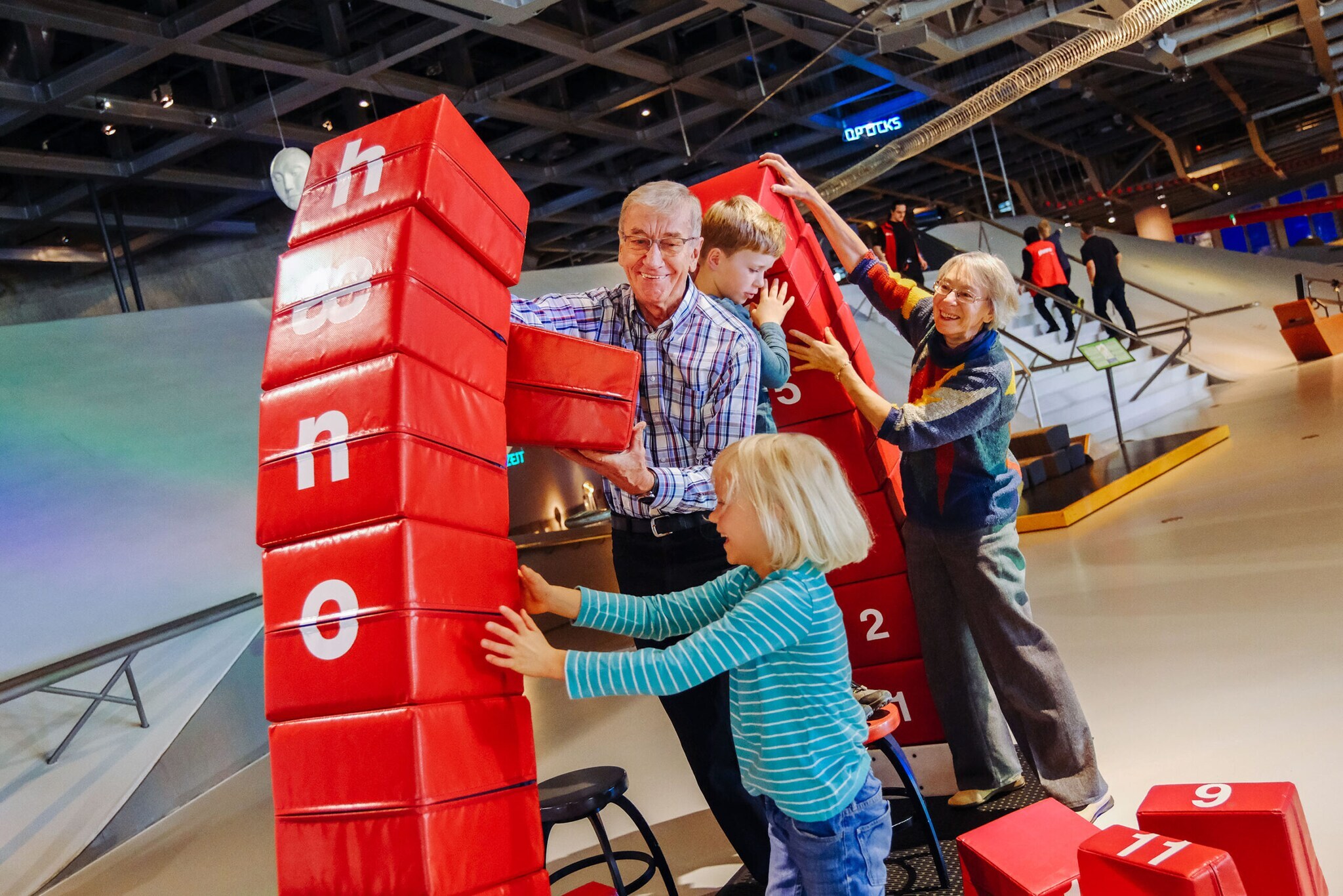 Zwei Kinder und ihre Großeltern bauen einen Brückenbogen aus Schaumstoffelementen in einem Bildungszentrum