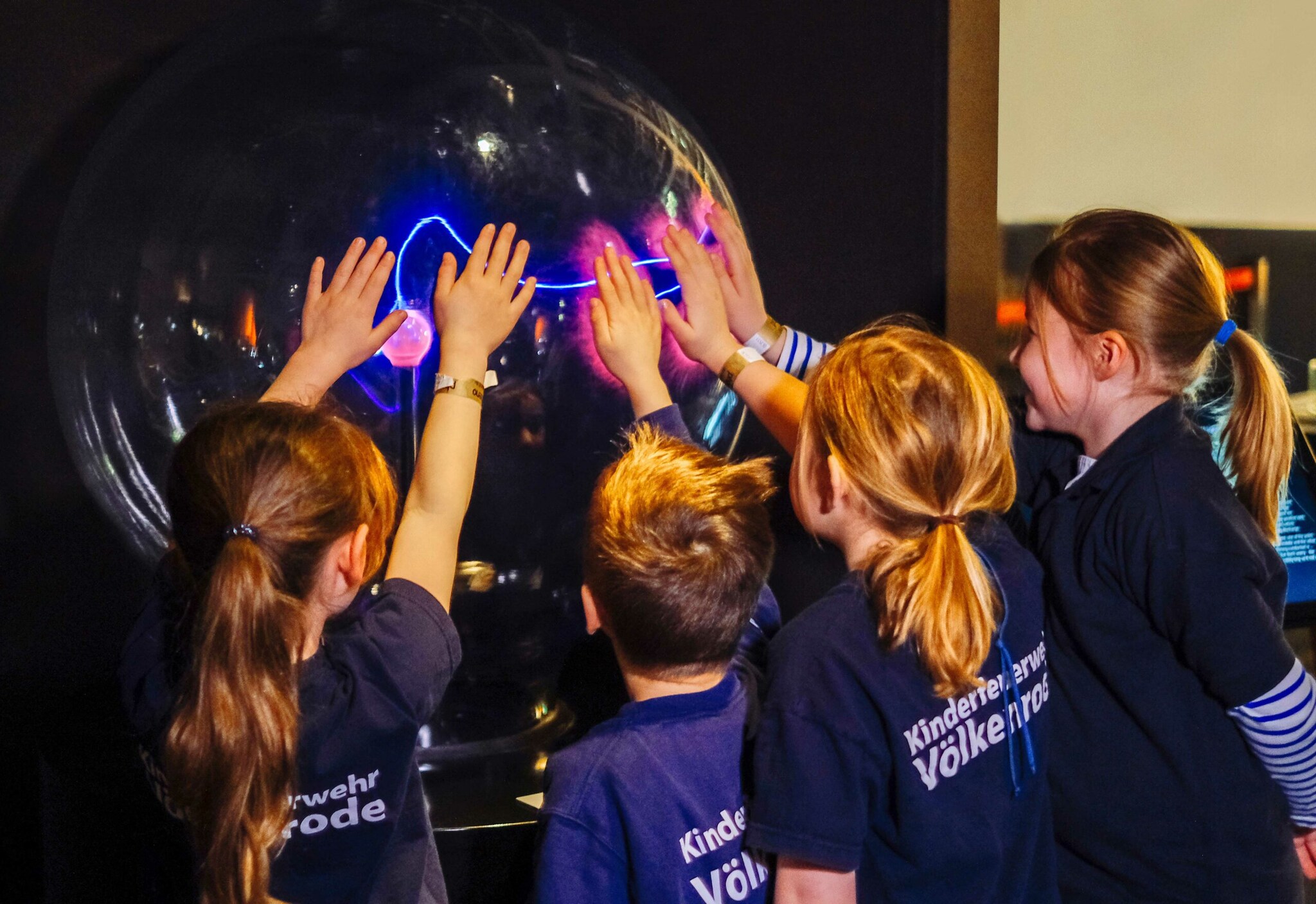 Vier Kinder legen ihre Hände auf eine Plasmakugel