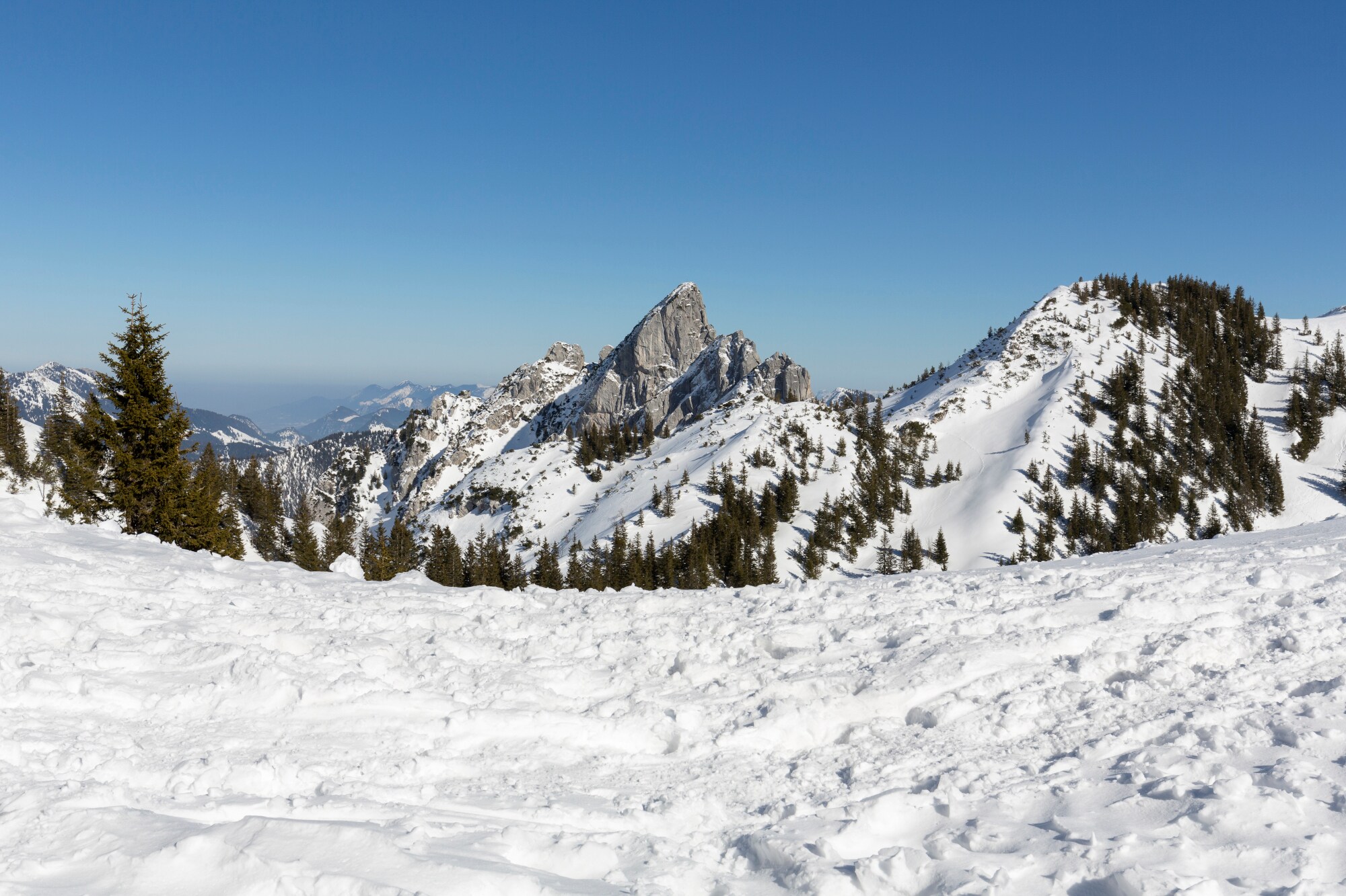 Blick auf die teilweise verschneiten Gipfel des Mangfallgebirges bei blauem Himmel