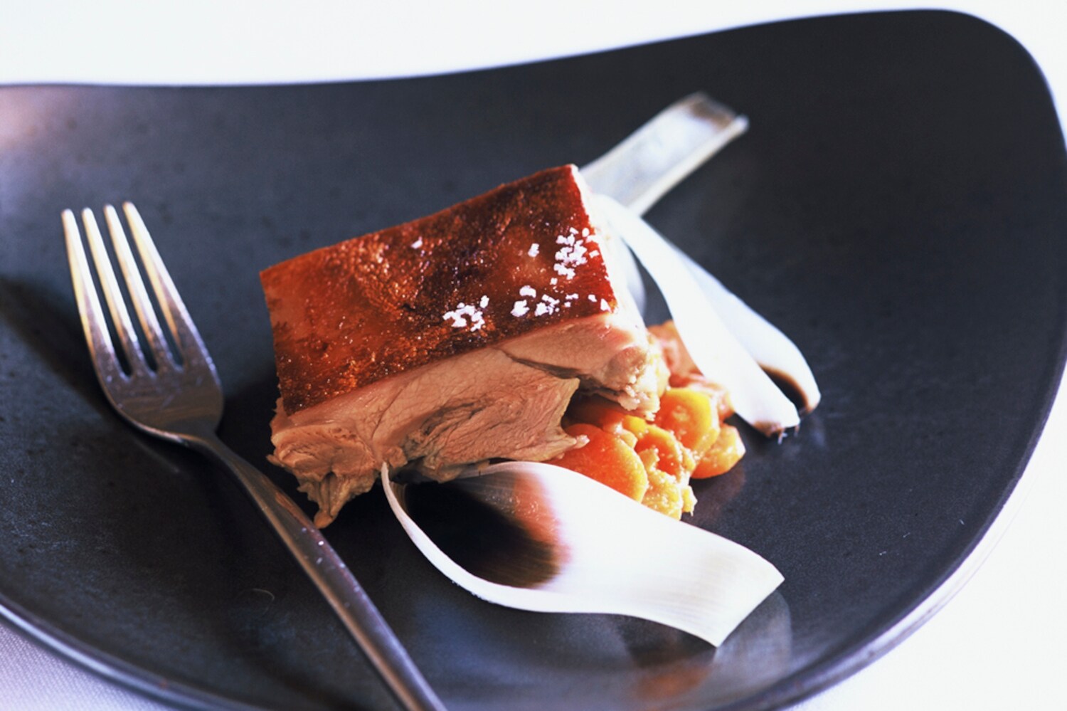 Ein Gericht mit einem Stück Fleisch und Gemüse und eine Gabel auf einem schwarzen Teller