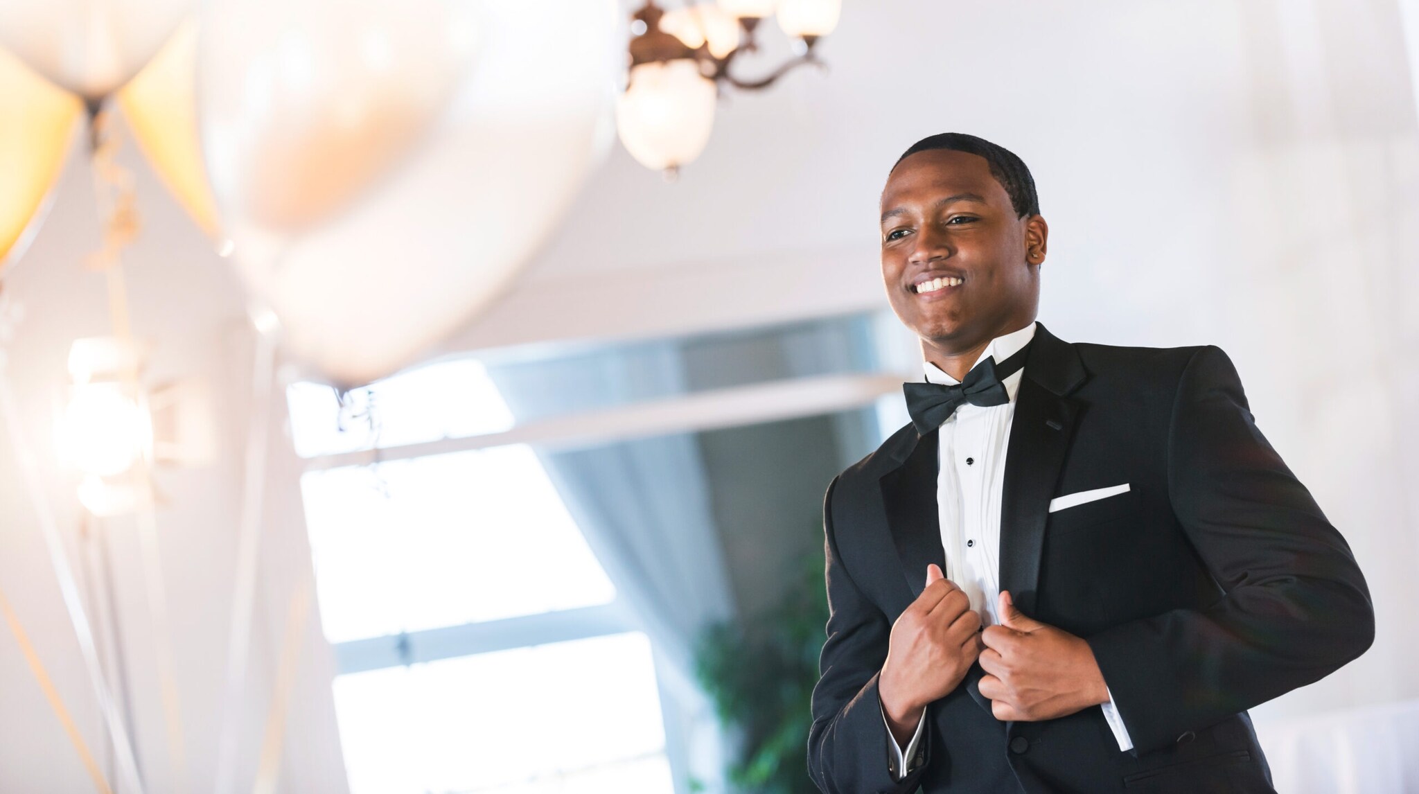 Ein Mann in schwarzem Smoking in einem weißen Raum mit Luftballons