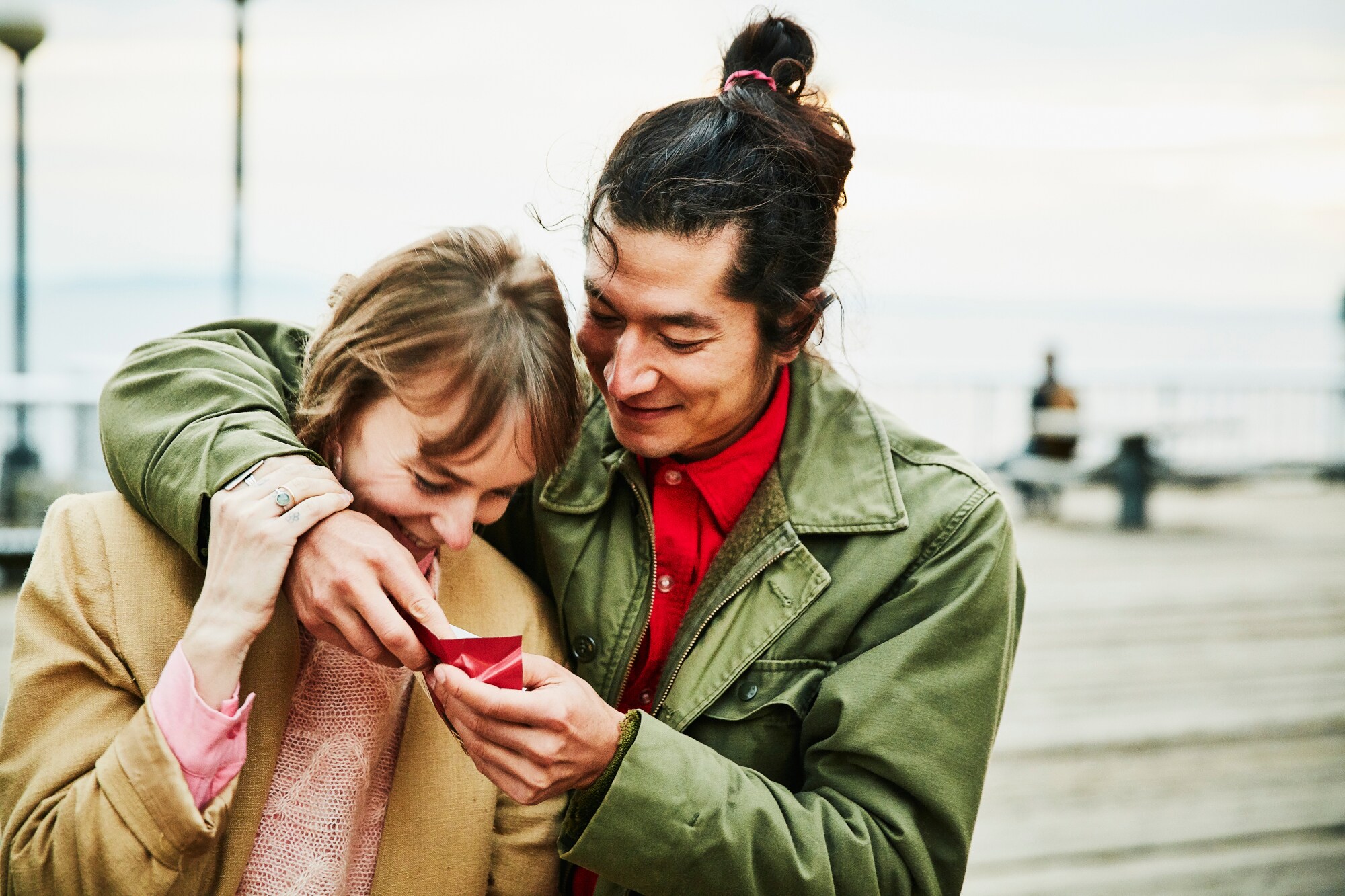 Ein lachendes, sich umarmendes Paar schaut gemeinsam auf eine kleine, rote Geschenkschachtel