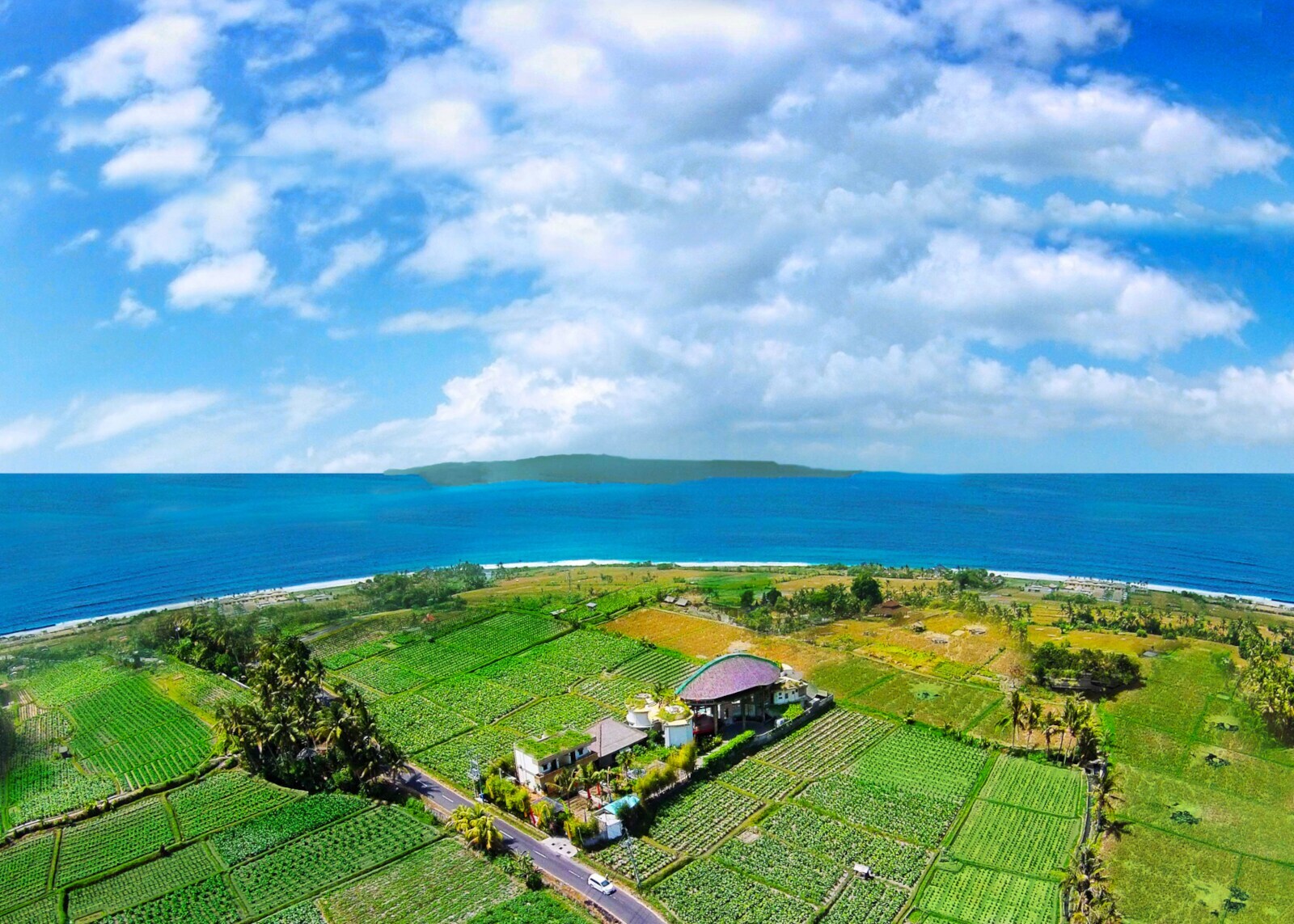 Zwischen grünen Feldern und dem Meer steht eine Hotelanlage auf Bali