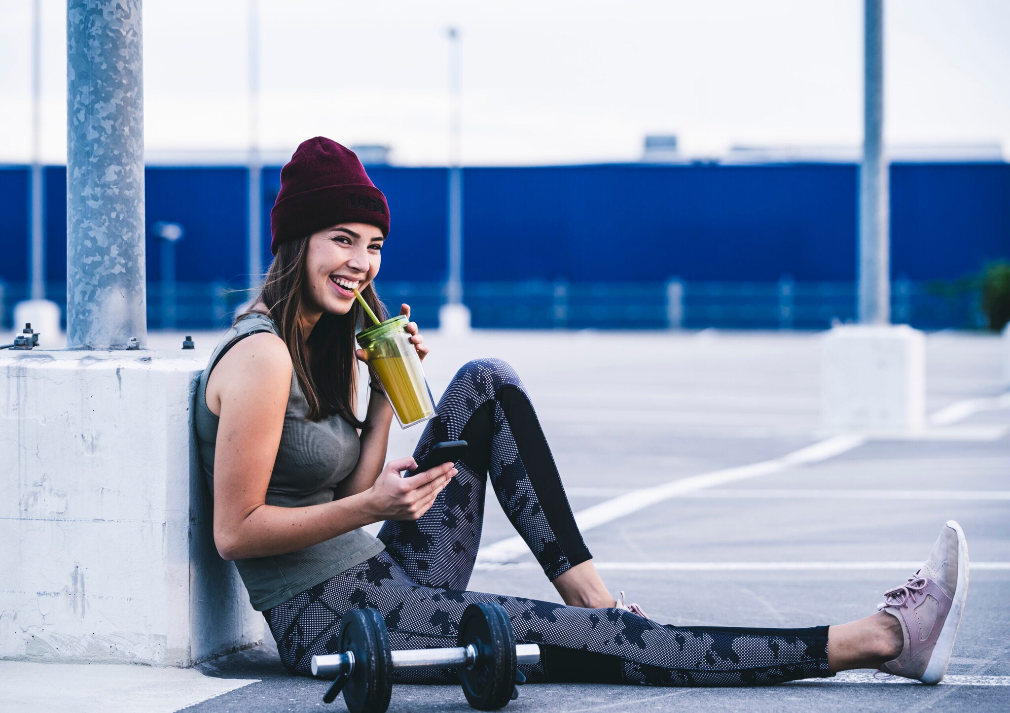 Eine junge Frau in Sportkleidung trinkt einen Smoothie, neben ihr liegt eine Hantel. Eine junge Frau in Sportkleidung trinkt einen Smoothie, neben ihr liegt eine Hantel.