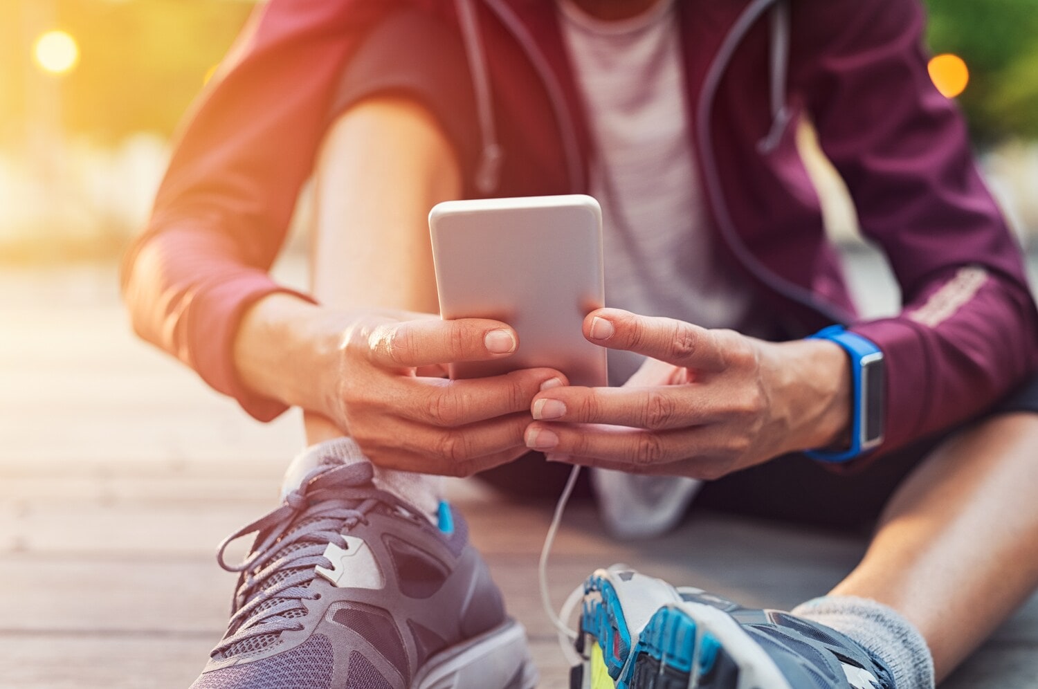 Sportlich gekleidete Person sitzt auf dem Boden und hält ein Handy in der Hand. Sportlich gekleidete Person sitzt auf dem Boden und hält ein Handy in der Hand.