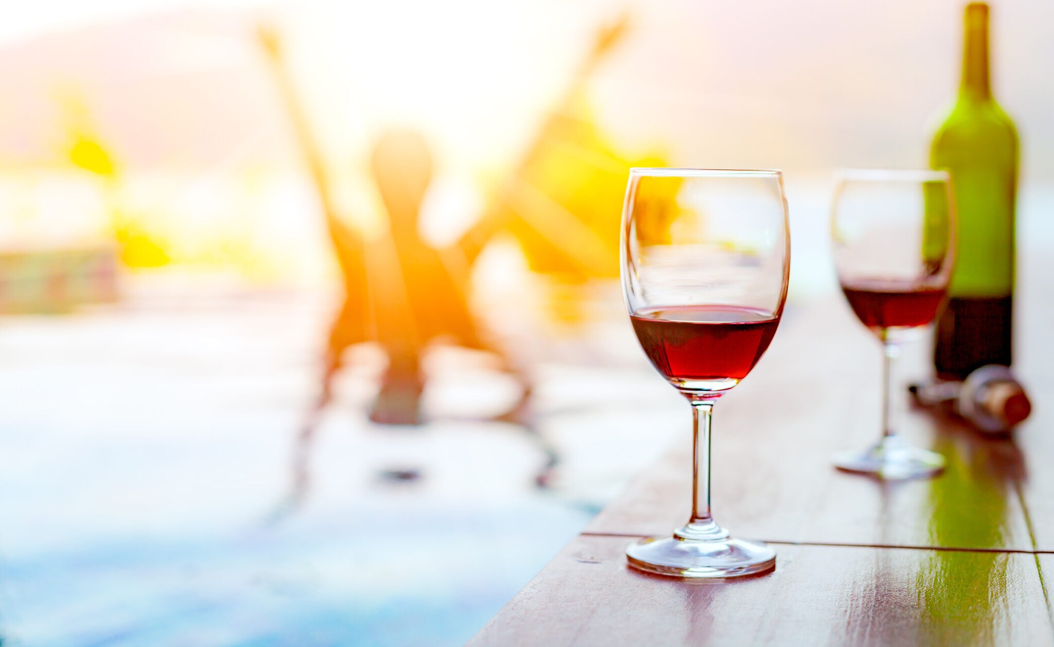 Zwei Gläser Rotwein stehen am Rand eines Schwimmbeckens.